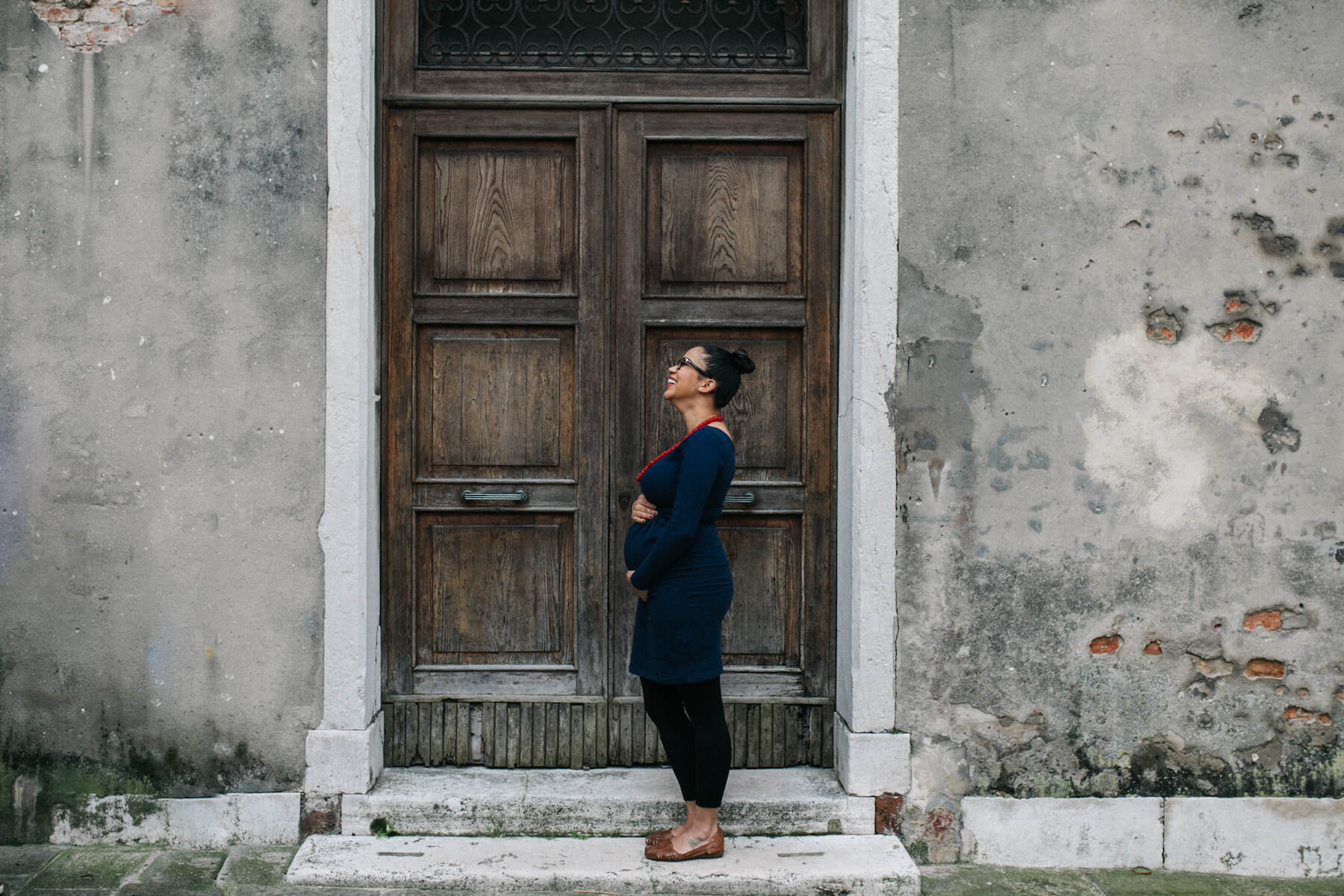 A pregnant woman is standing in front of an old door in Venice, Italy