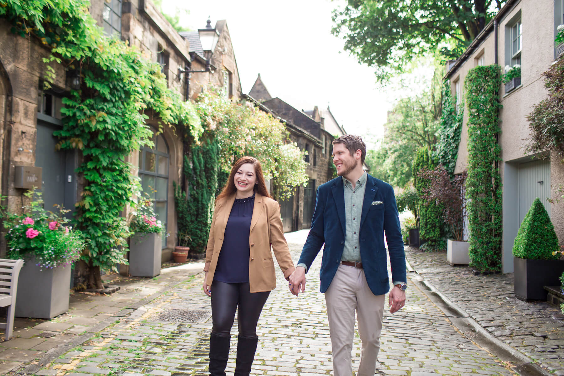 a couple holding hands and walking on a cobble street in Edinburgh, Scotland