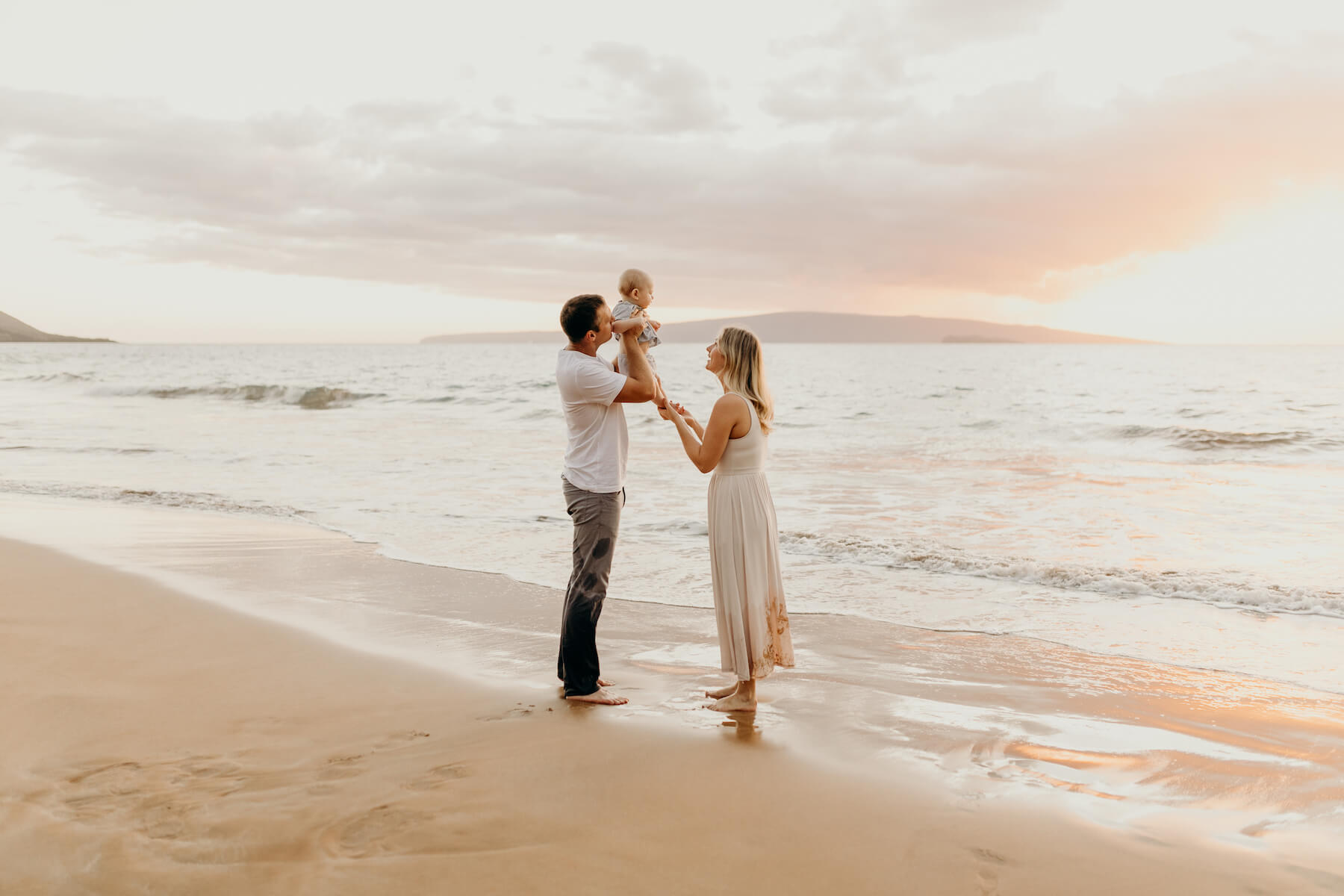 family of three with a baby boy, holding the child and playing on the beach in Maui, Hawaii