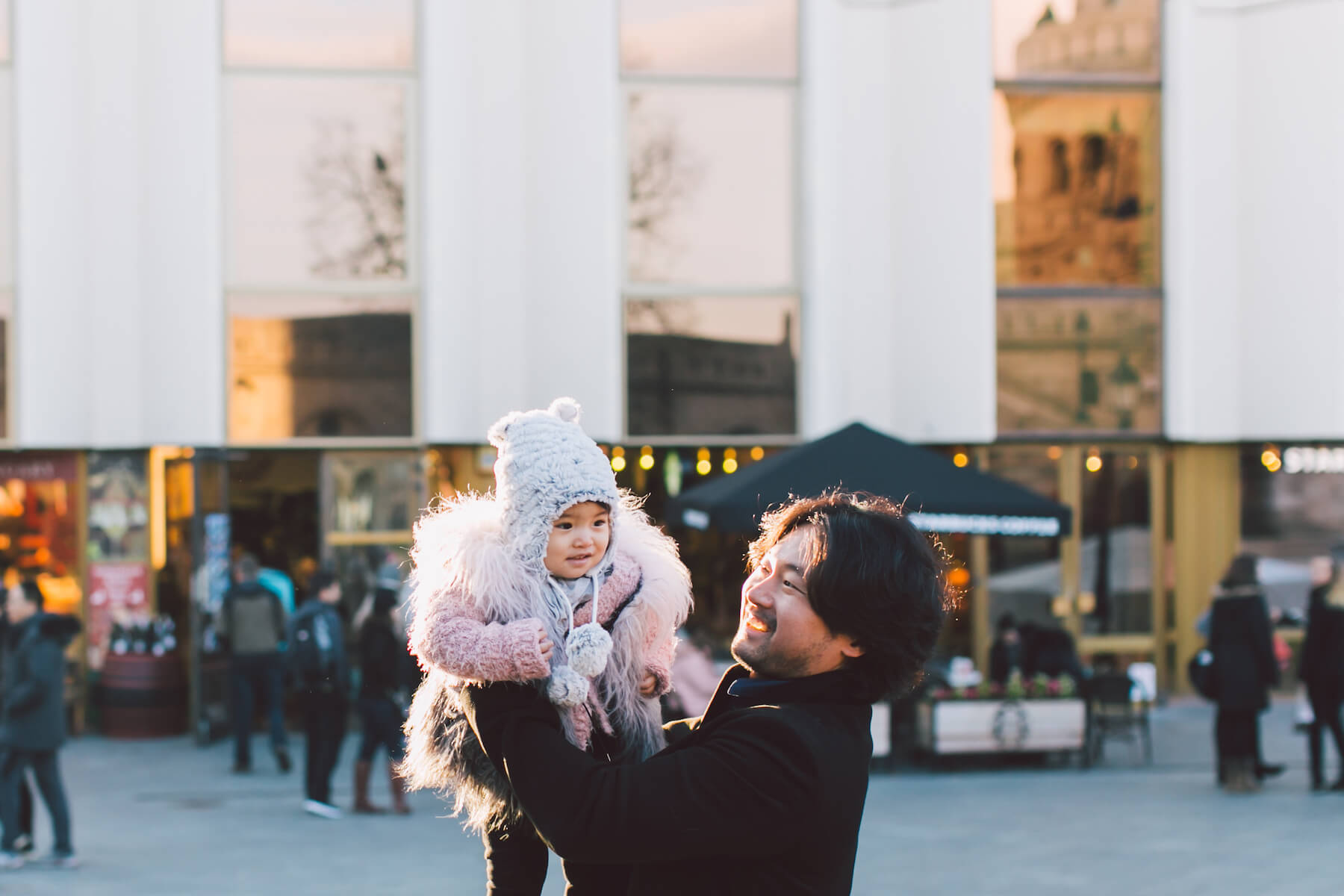 father holding a baby girl up in the air in a city square in Budapest, Hungary