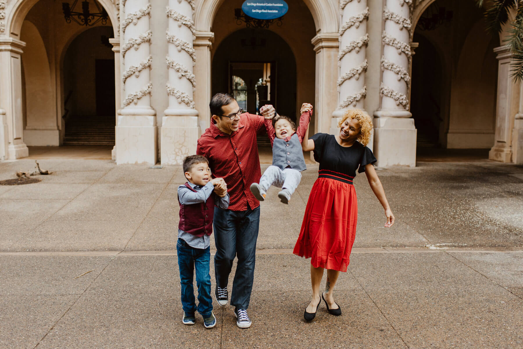 a family with two young children, holding hands and one child is being lifted, laughing in San Diego, California