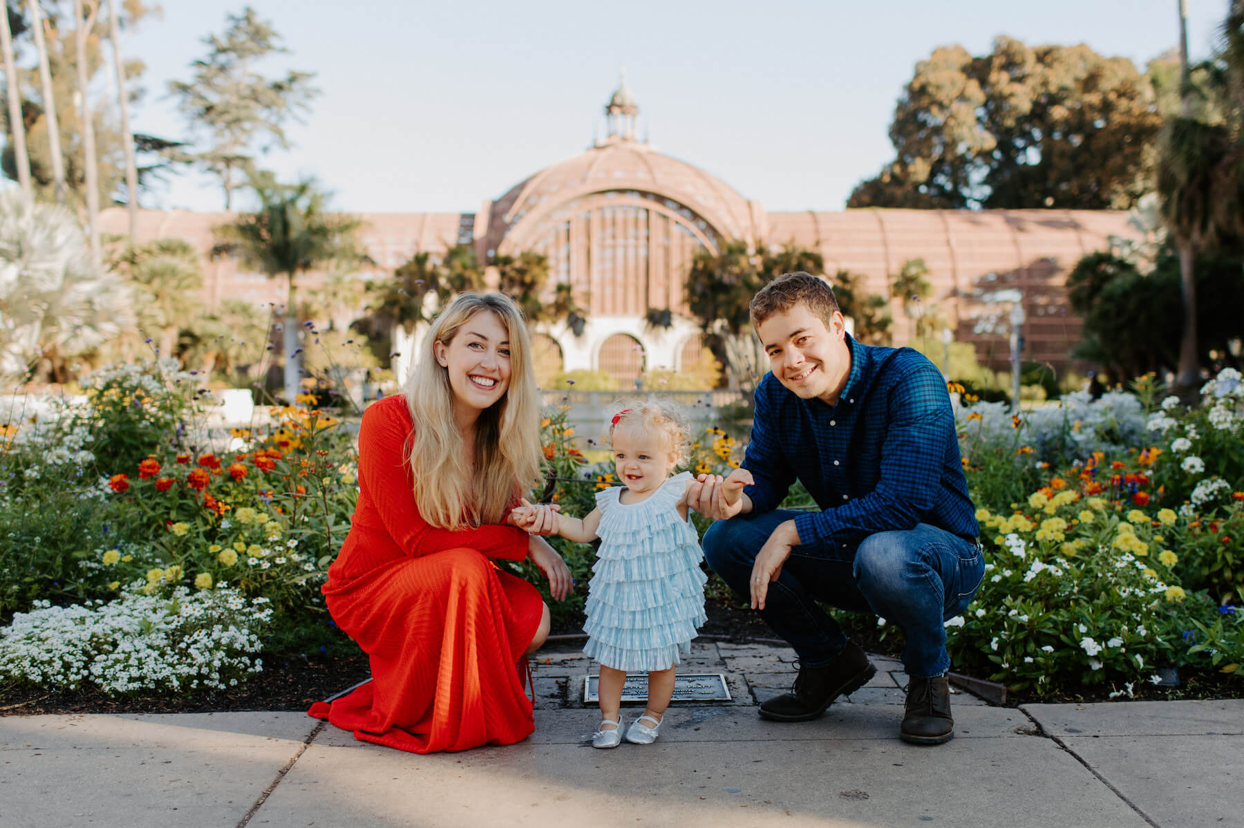 a family with a little girl, kneeling and smiling in front of a garden in San Diego, California