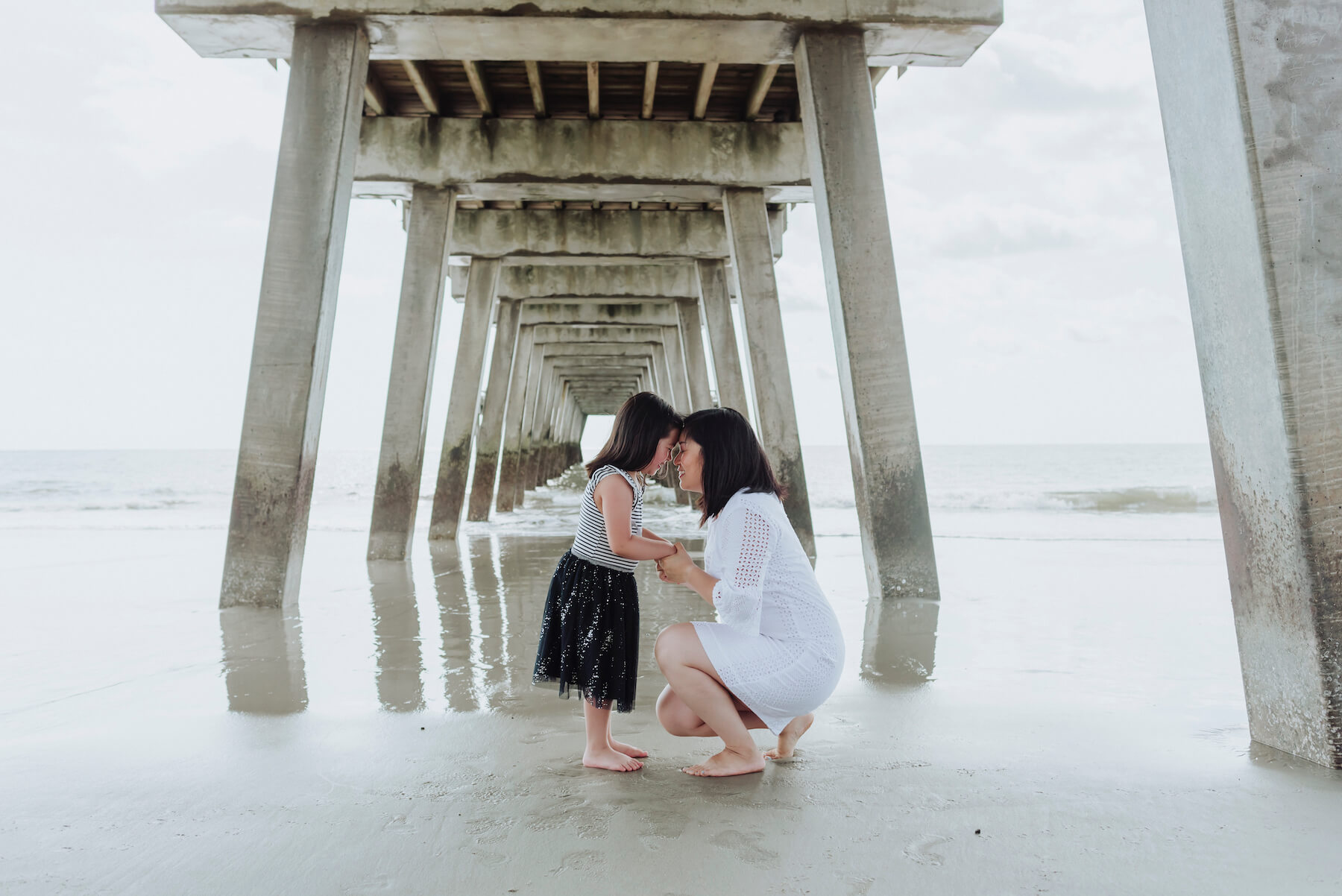 mother and daughter kneeling down under the beach pier in Savannah, Georgia, United States of America
