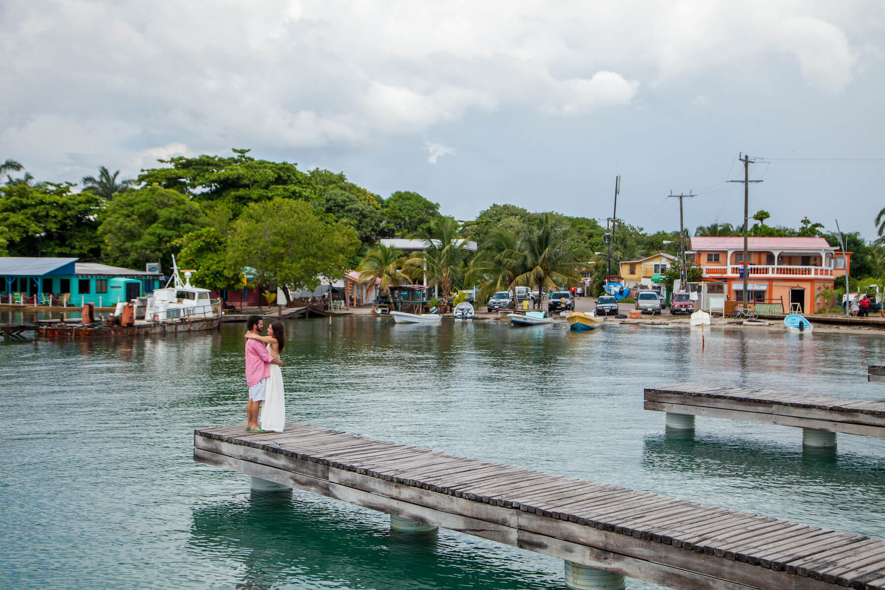 couple holding each other on a dock with the village of Placencia, Belize in the background
