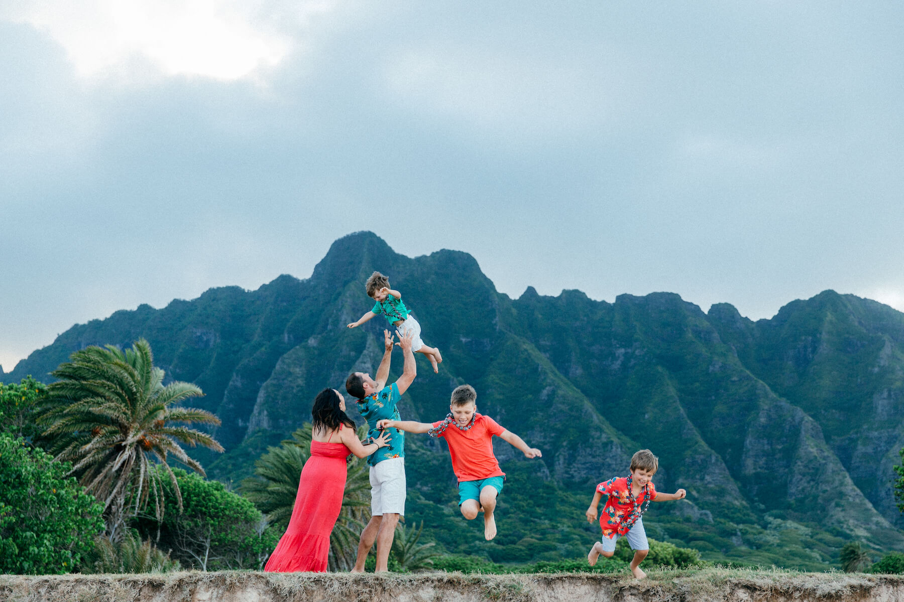 family of five, the three sons are jumping off a small ledge on the beach in Honolulu, Hawaii
