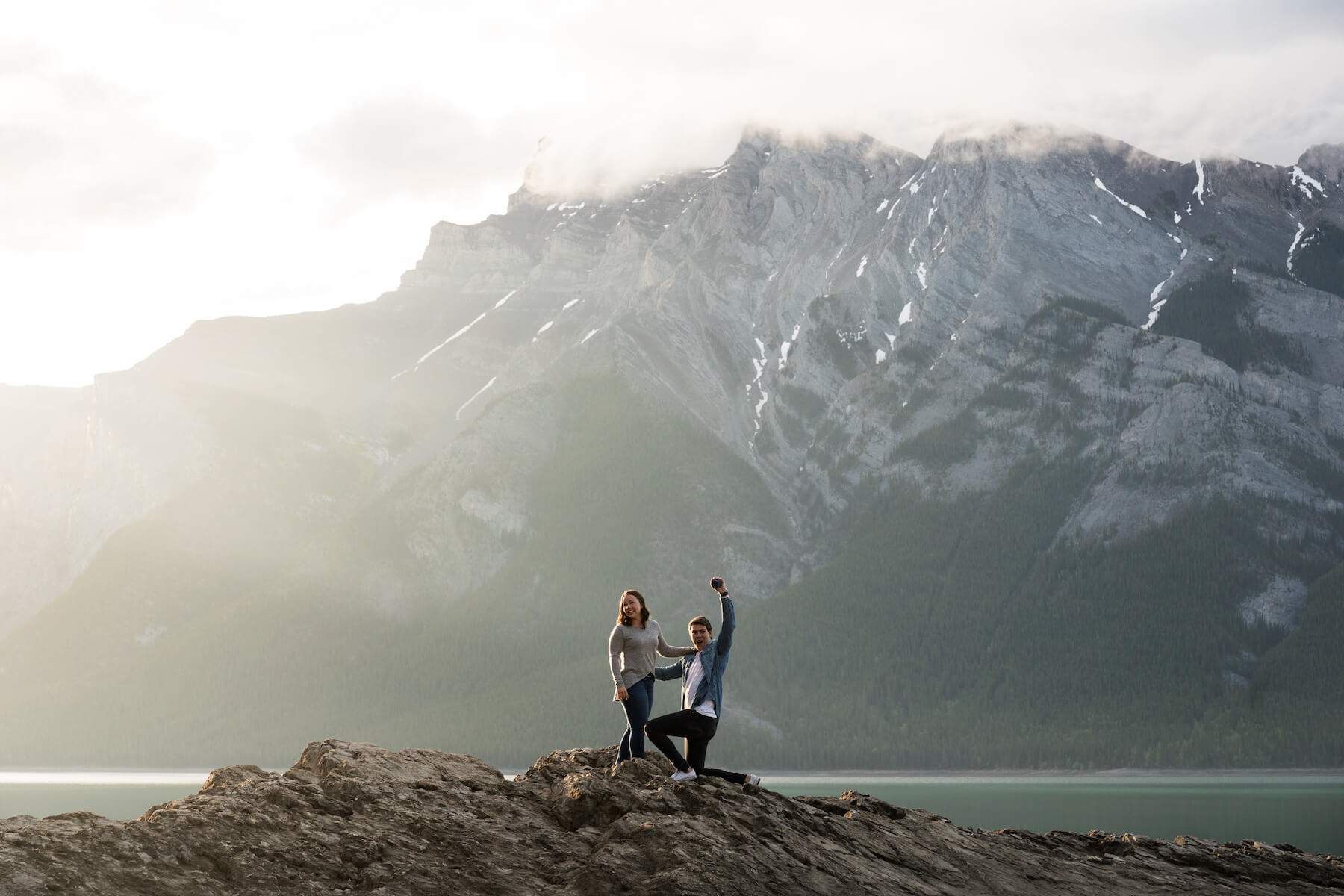 a man is proposing to the woman and he is raising his arms in the air in Banff, Canada