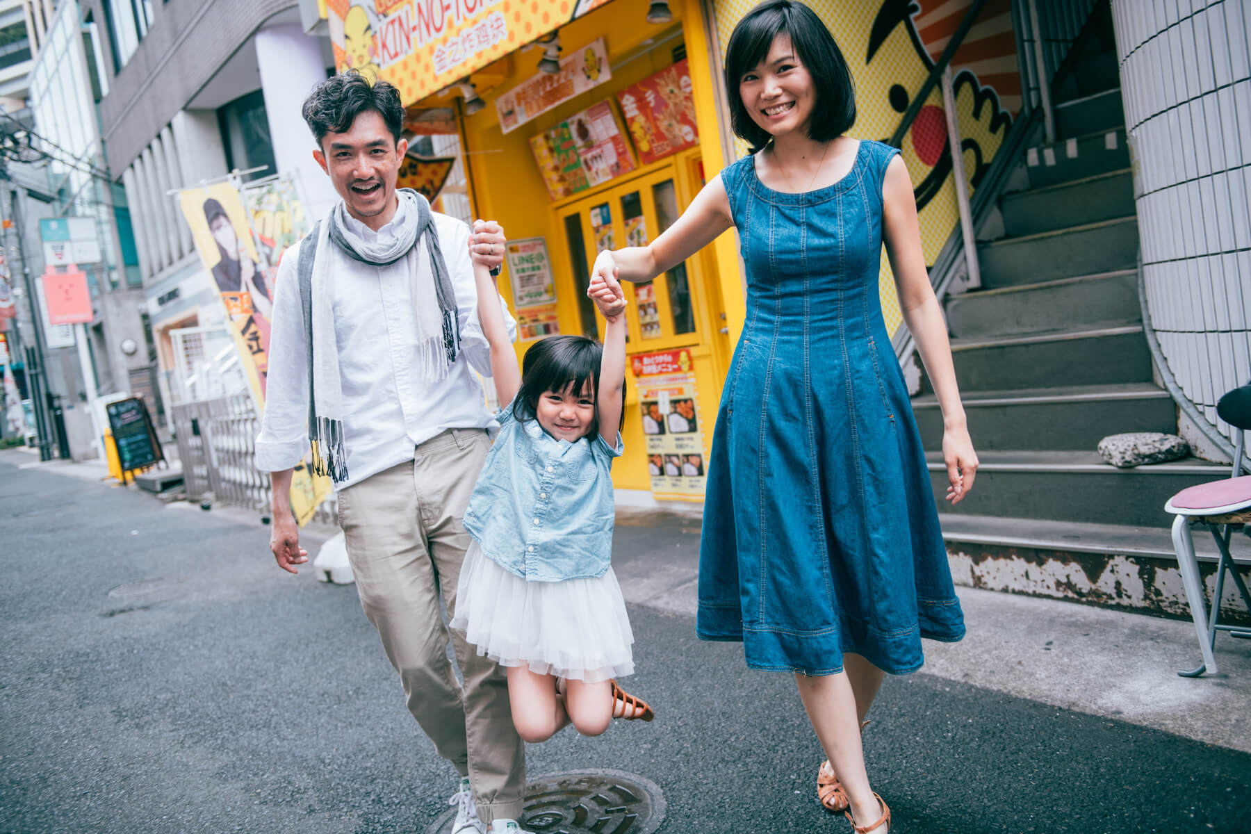 family of three, the parents are swinging the girl in the air while they are walking in Tokyo, Japan