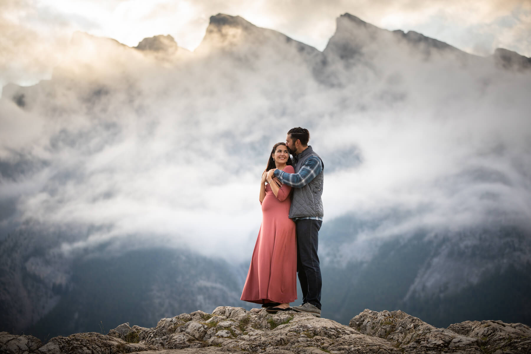 pregnant couple holding each other in an embrace near the lake in Banff, Alberta, Canada