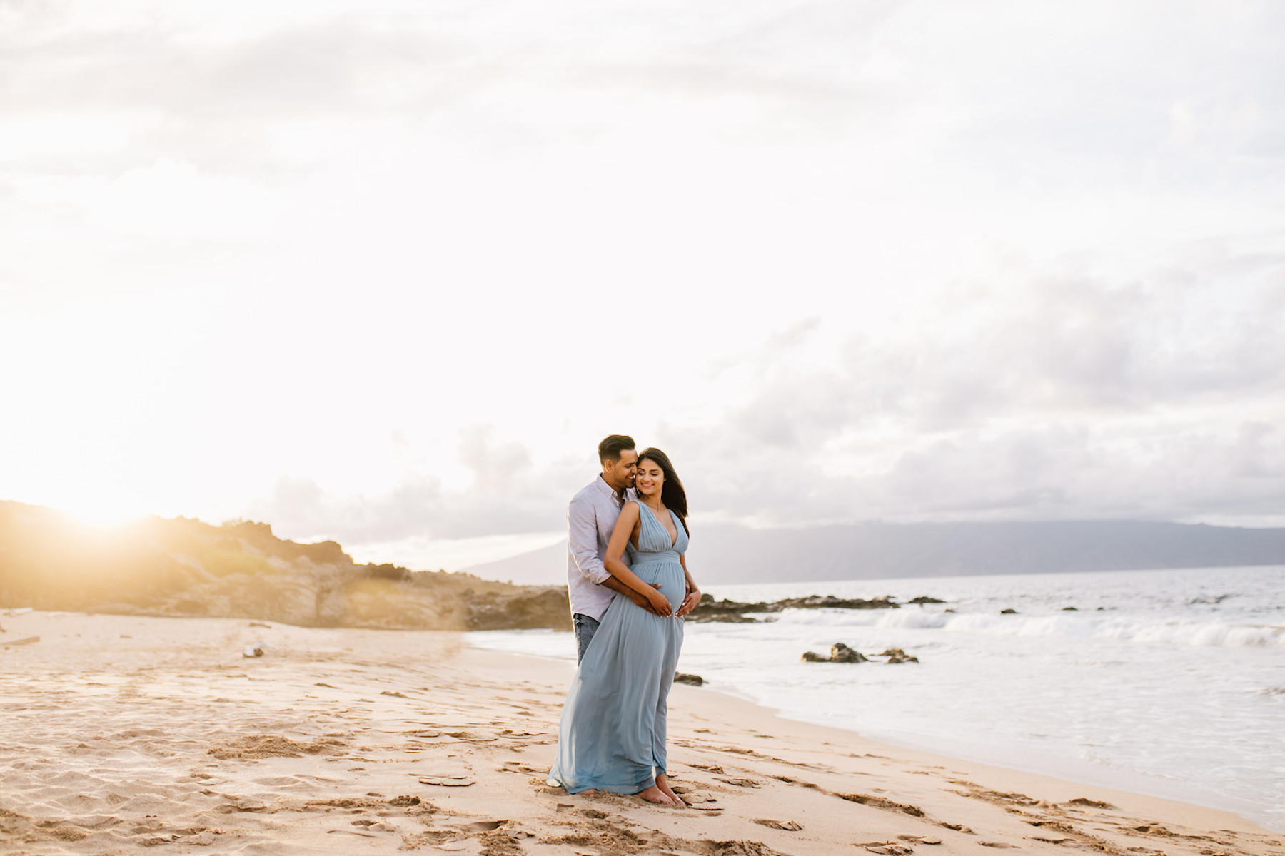 pregnant couple holding each other on the beach in Maui, Hawaii
