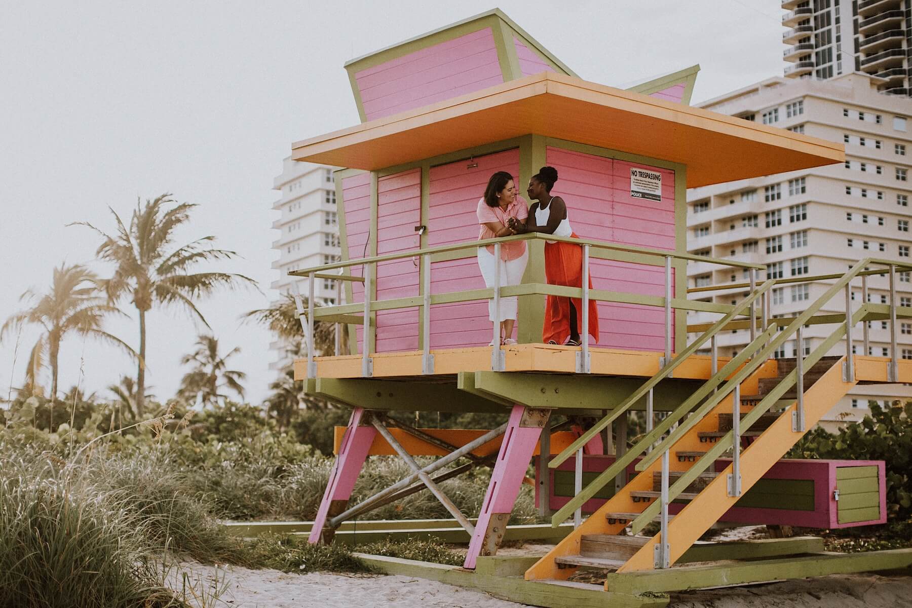LGBTQ couple looking at each other while standing a lifeguard tower in Miami, Florida