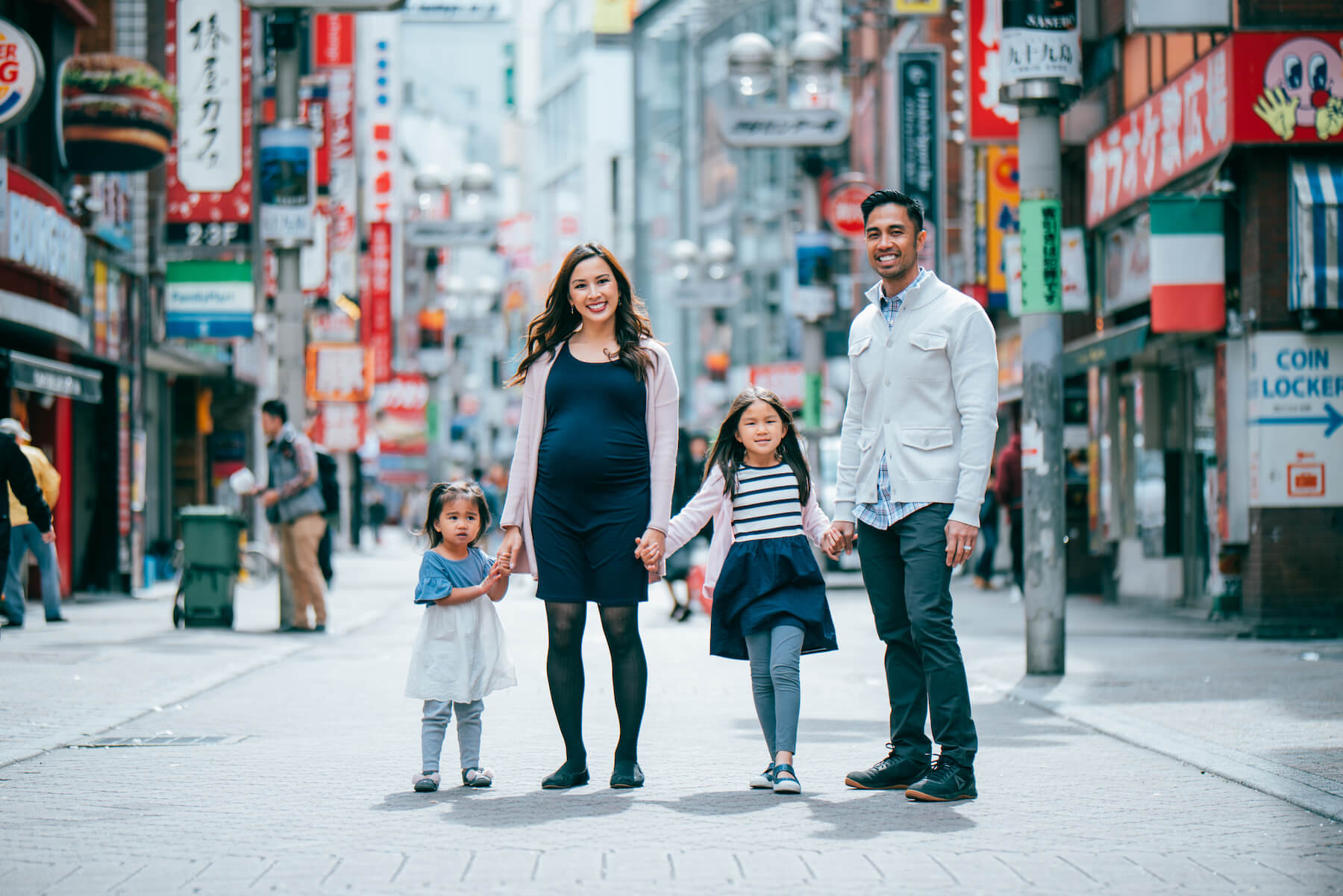 a family of 4, and the mother is pregnant, standing on the street holding hands in Tokyo, Japan
