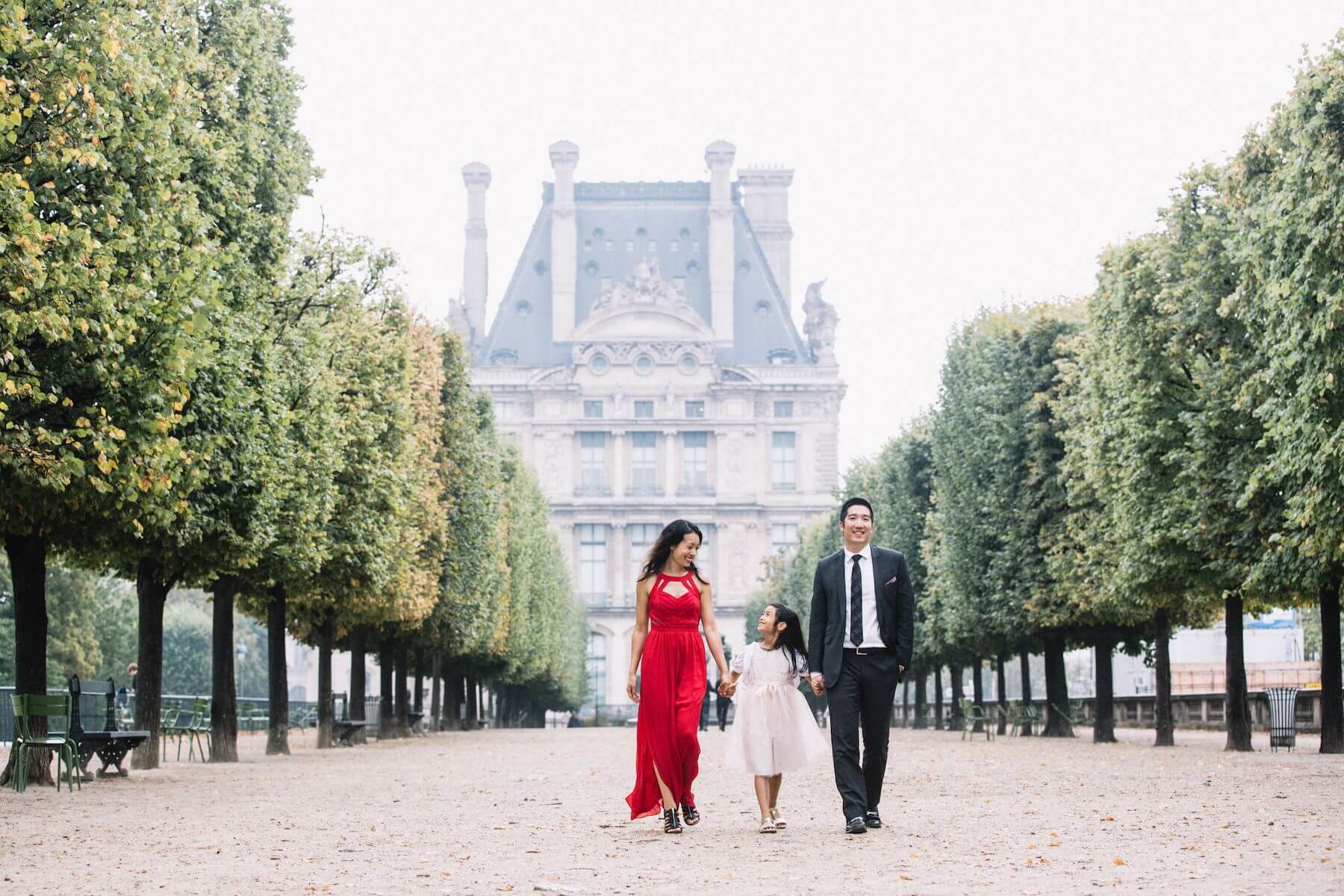 a family of three holding hands and walking in the gardens near the Louvre in Paris, France