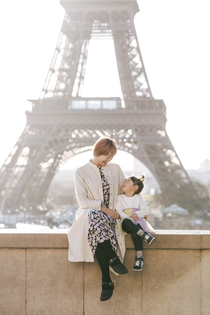 mother and daughter sitting on a ledge and behind them is the Eiffel Tower in Paris, France