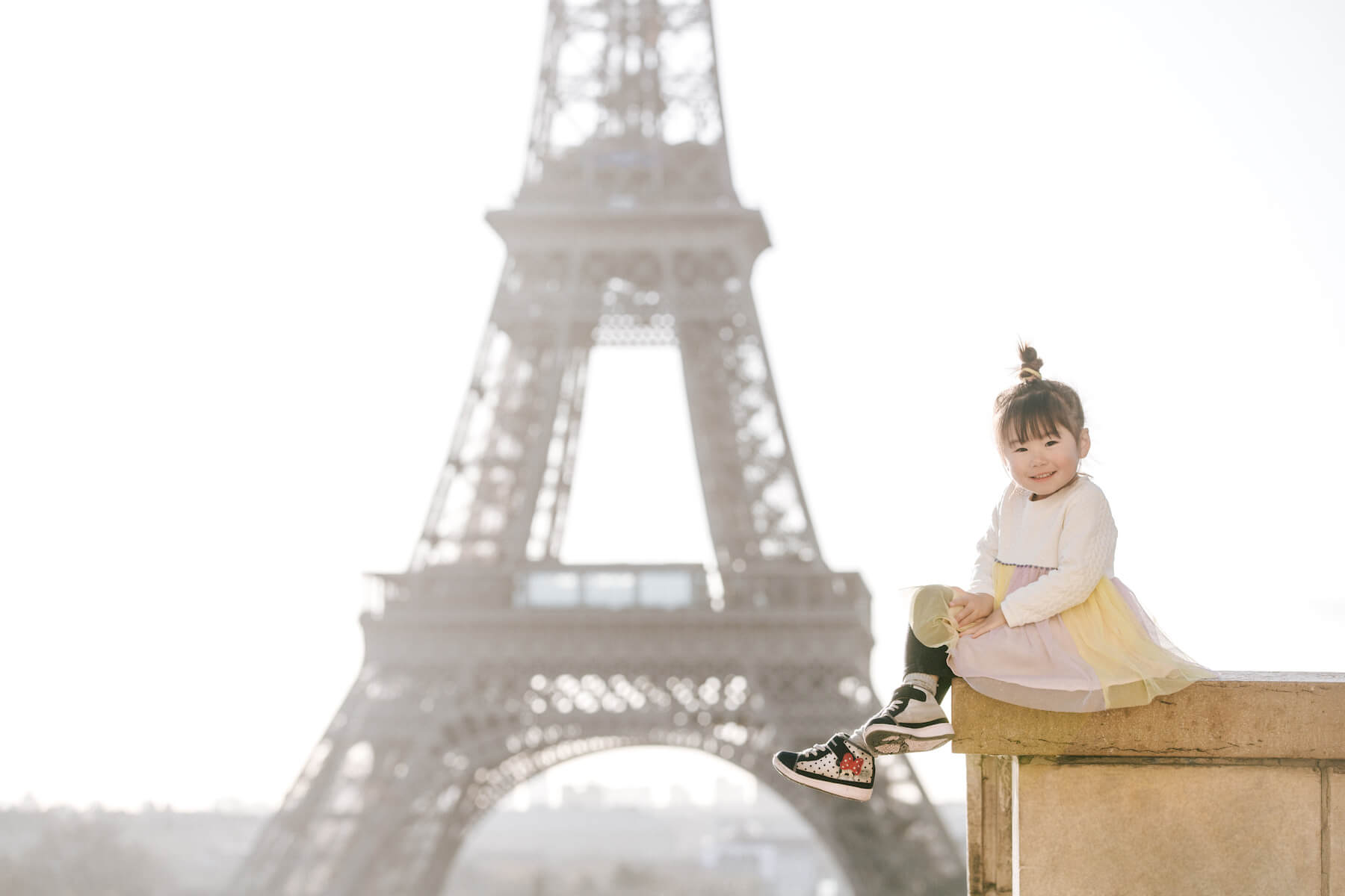 a small girl sitting on a ledge with the Eiffel Tower in the background in Paris, France