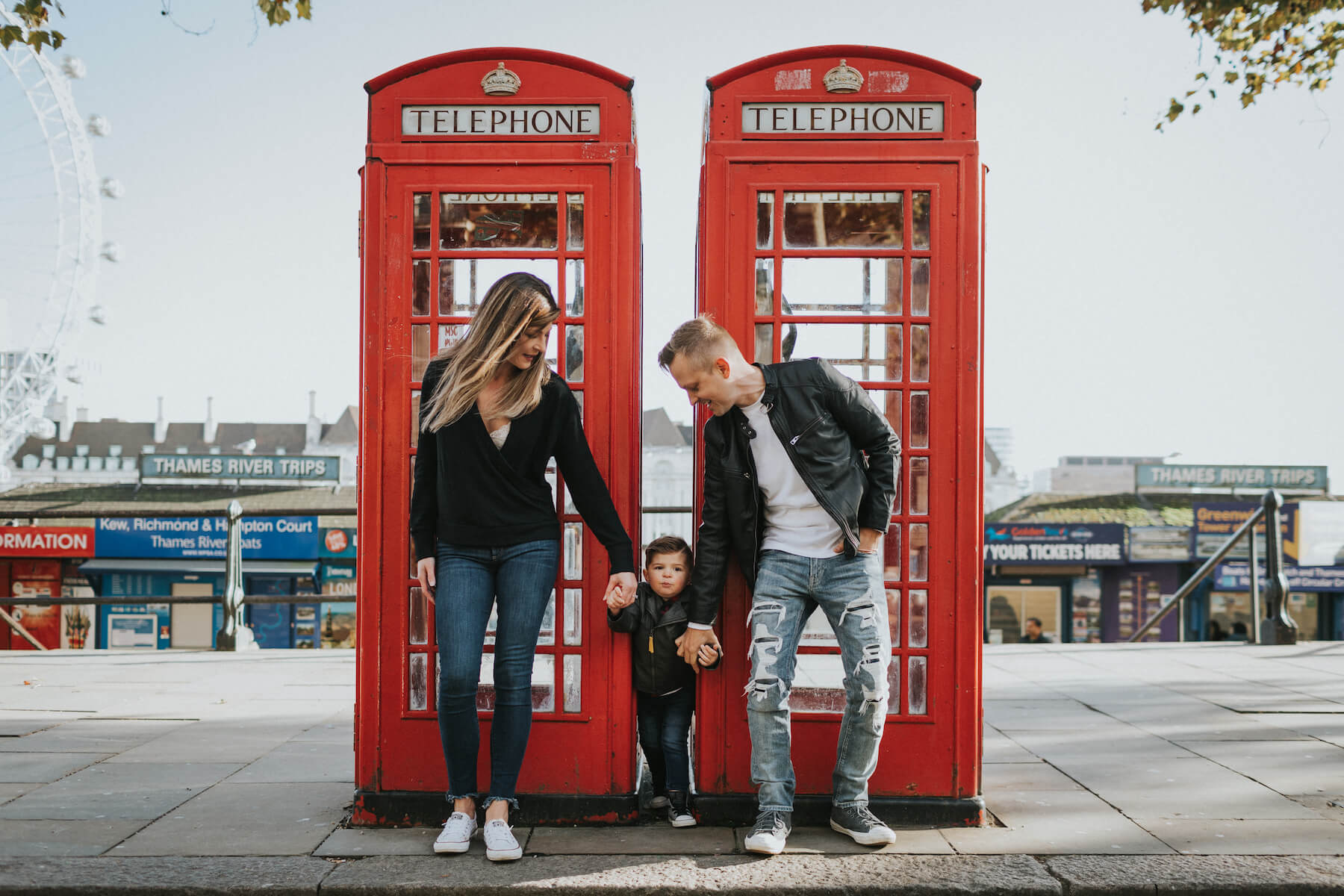 a family of three standing by a red phone booth in London, England
