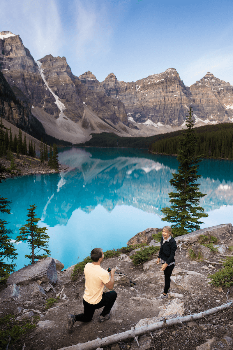 man proposing to a woman standing on a hilltop with a beautiful lake in the background in Banff, Alberta, Canada