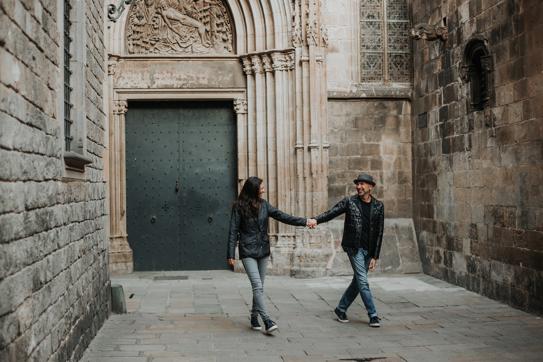 couple holding hands and running through a courtyard full of pigeons in the Gothic District in Barcelona, Spain