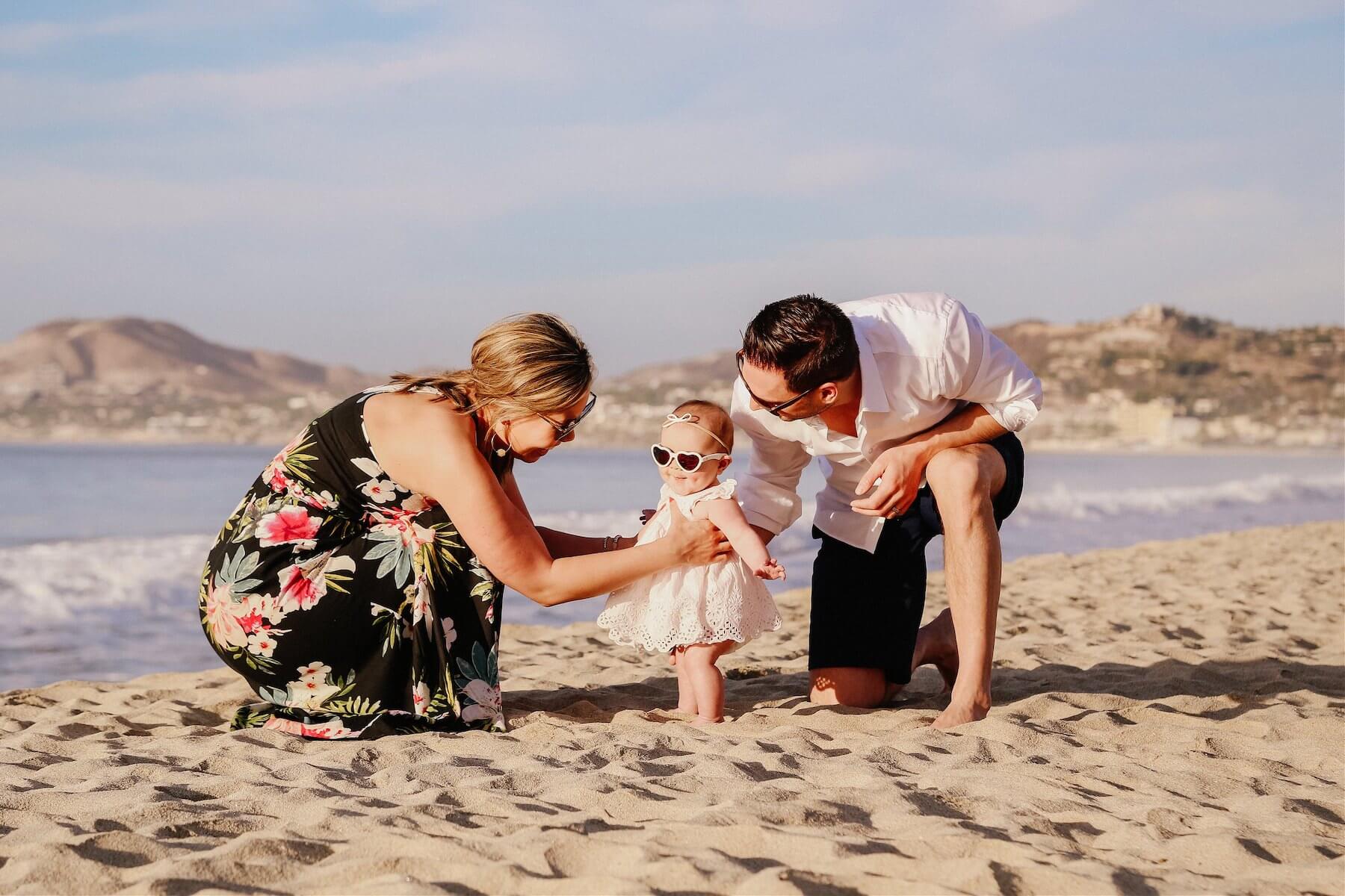 family of three, the baby is wearing sunglasses and sitting on the beach in Cabo San Lucas, Mexico