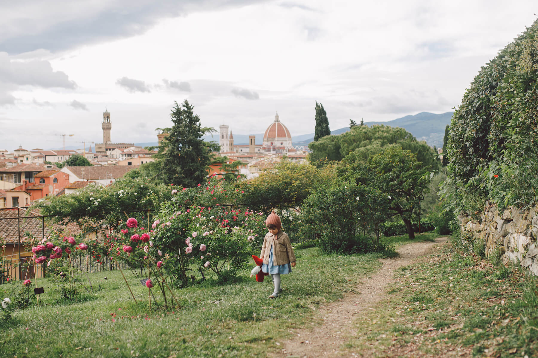 a little girl is holding a toy and walking in a garden in Florence, Italy