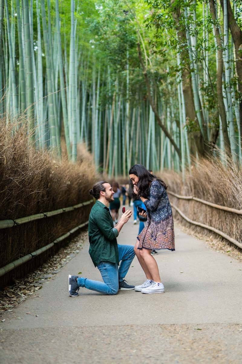 a man is kneeling in the bamboo forest and proposing to a woman in Kyoto, Japan