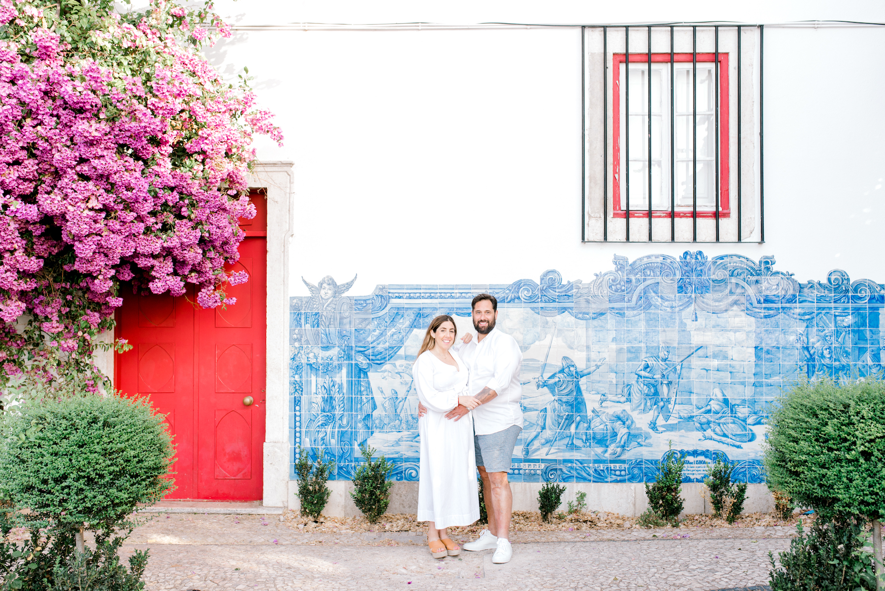 pregnant couple standing in front of a colourful building in Lisbon, Portugal