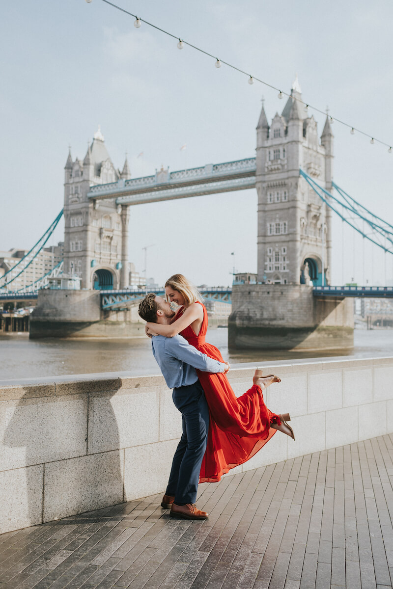 a man is lifting a woman in front of the tower bridge in London, England