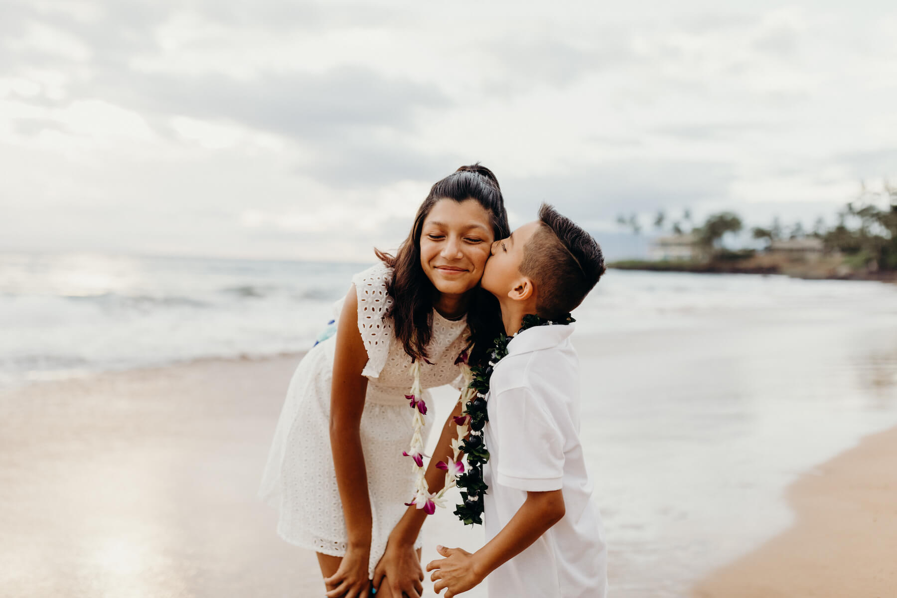 brother is kissing his sister on the cheek on the beach in Maui, Hawaii