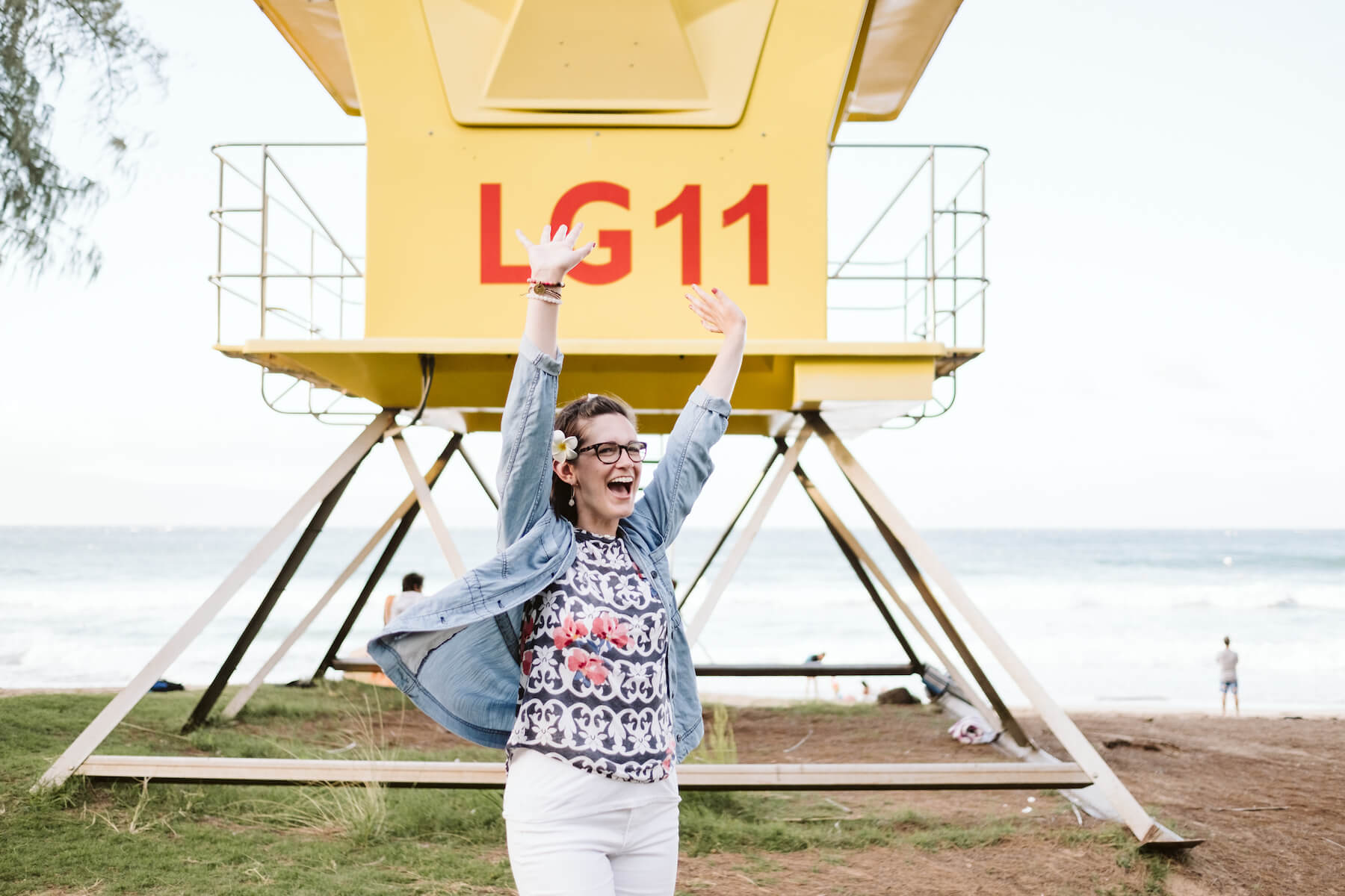 solo traveller standing in front of a lifeguard station with her hands up in Maui, Hawaii