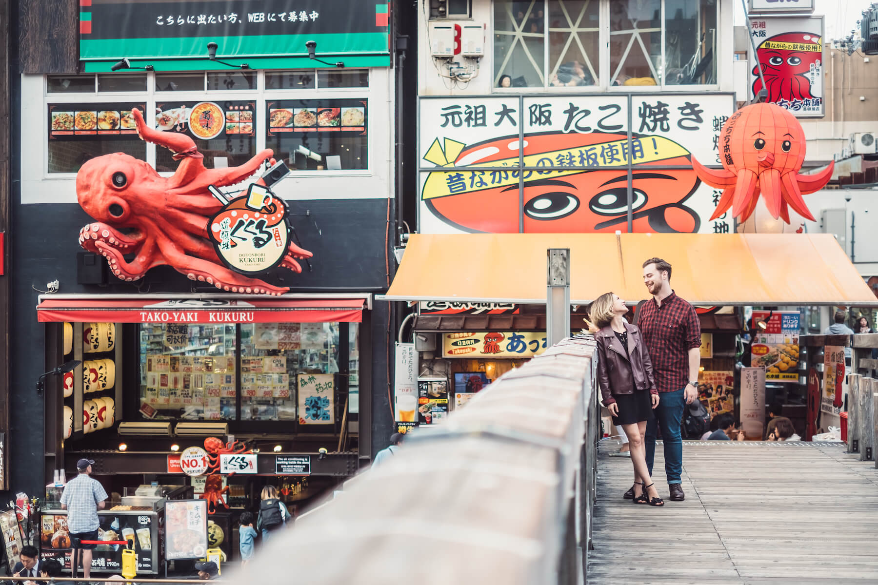 couple standing on a bridge with colorful buildings in the background in Osaka, Japan