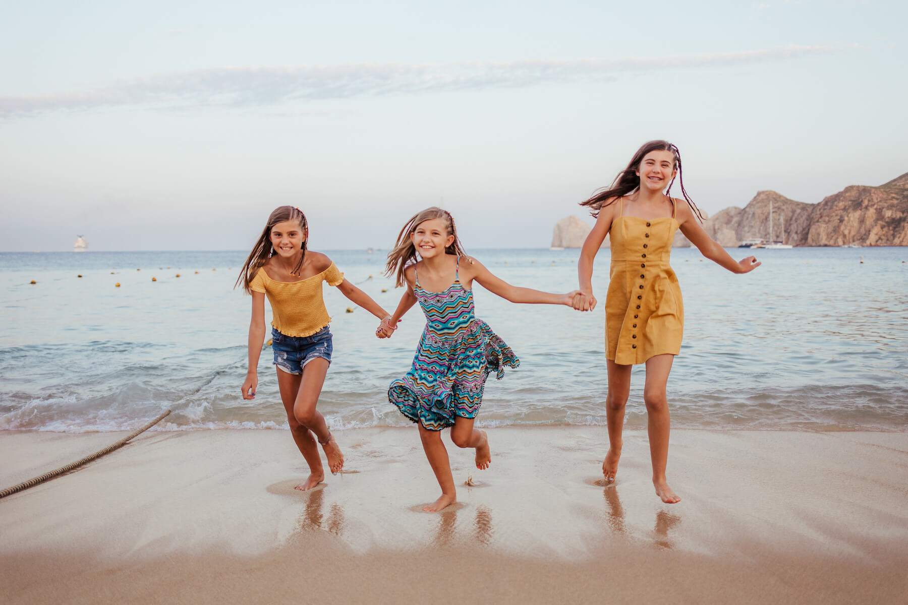 Three sisters holding hands and running on the beach in Cabo San Lucas, Mexico