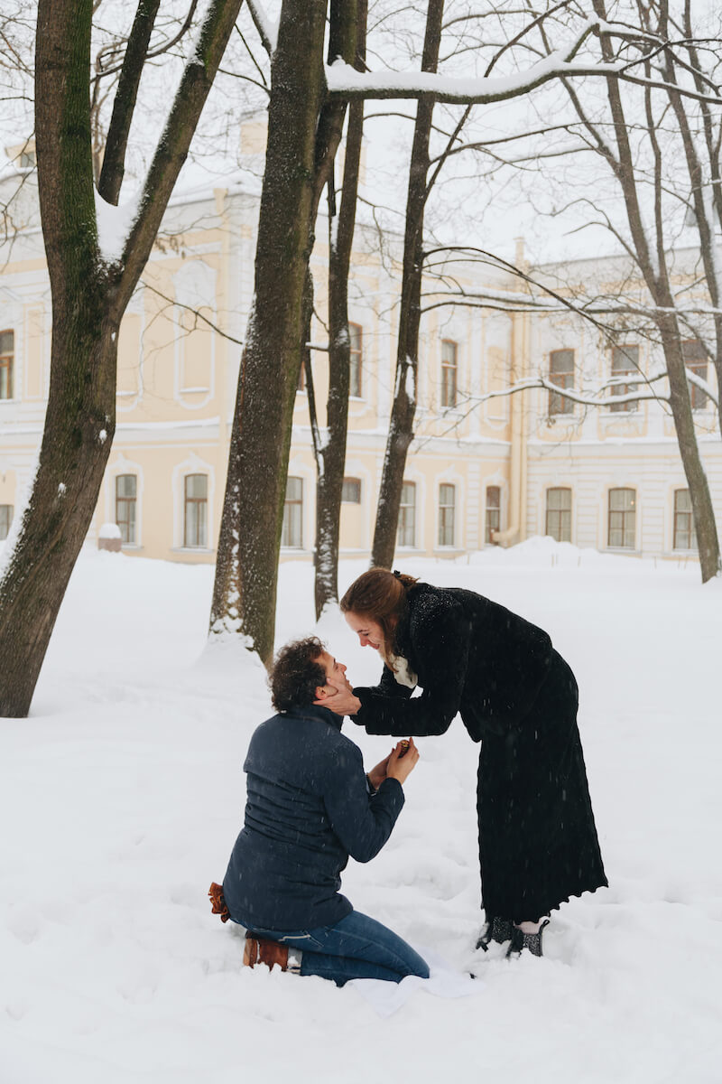 the man is proposing to the woman, he is kneeling in the snow and she is bending over with excitement in St. Petersburg, Russia