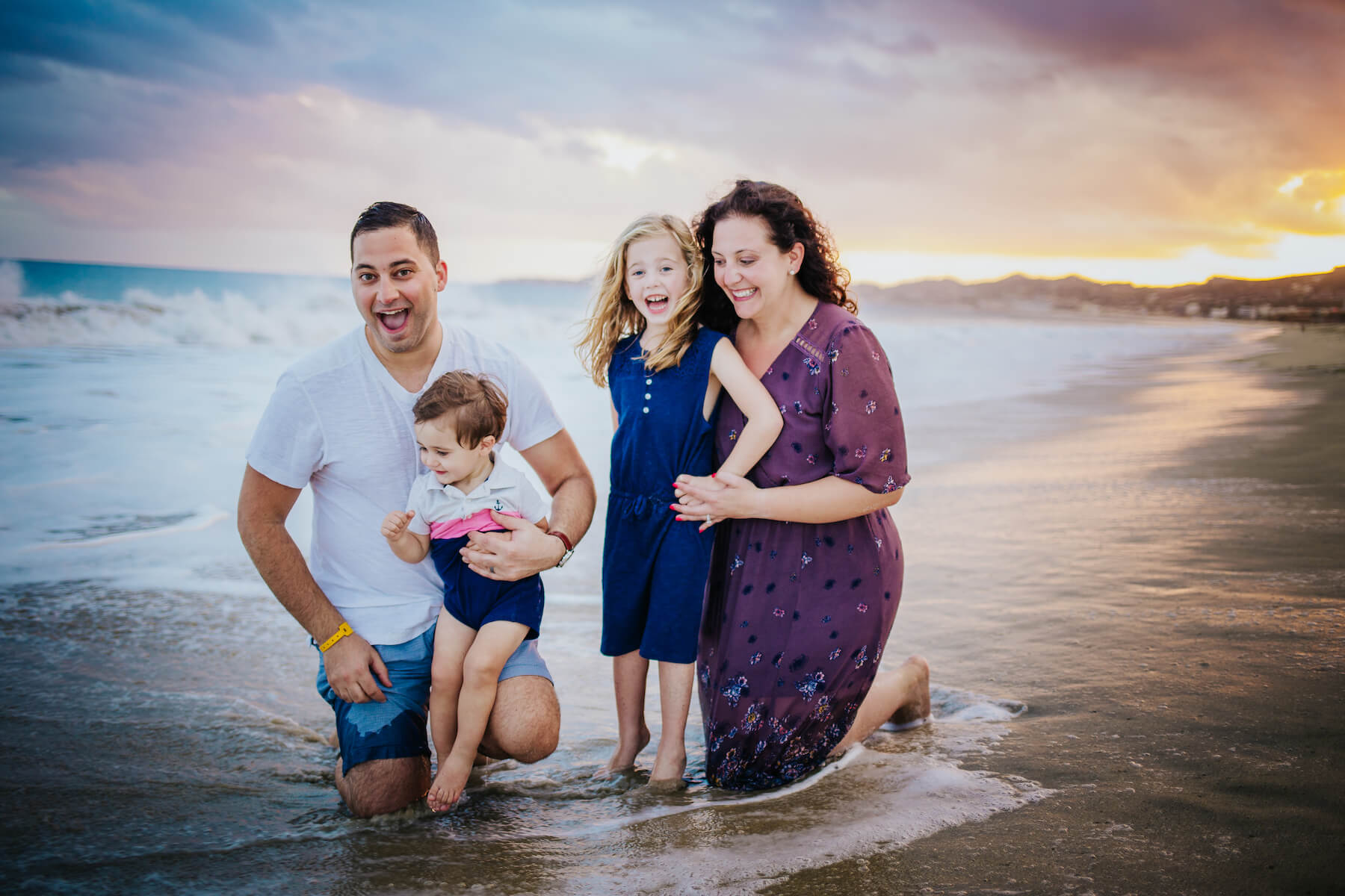 family of four sitting in the ocean and getting wet in Cabo San Lucas, Mexico