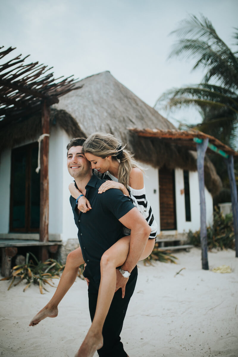 the man has the woman on his back and they are on the beach in Playa Del Carmen