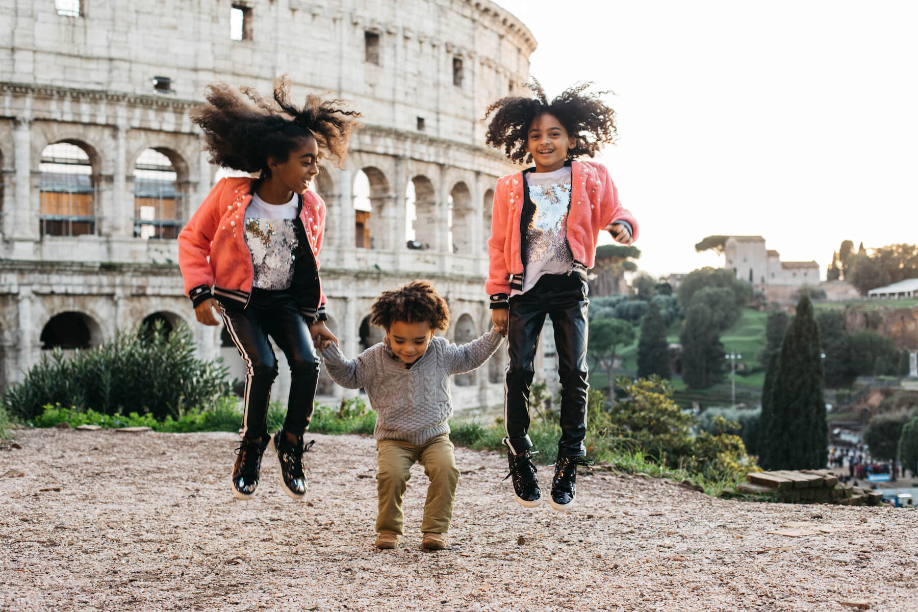 a brother and two sisters jumping in front of the colosseum in Rome, Italy