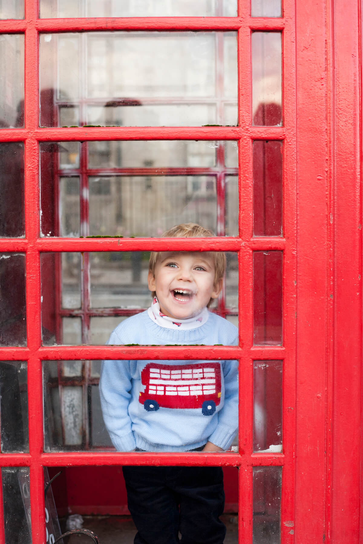 Boy laughing inside of a telephone booth in London England