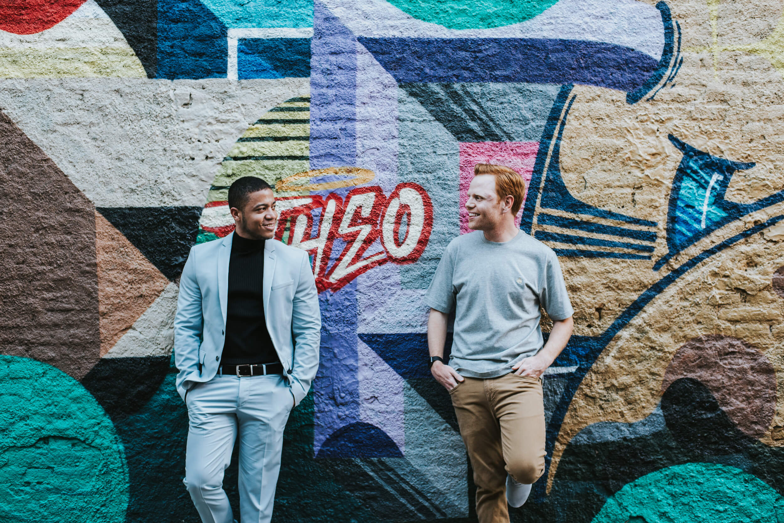 Two men stand in front of a colourful painted wall in Buenos Aires, Argentina.