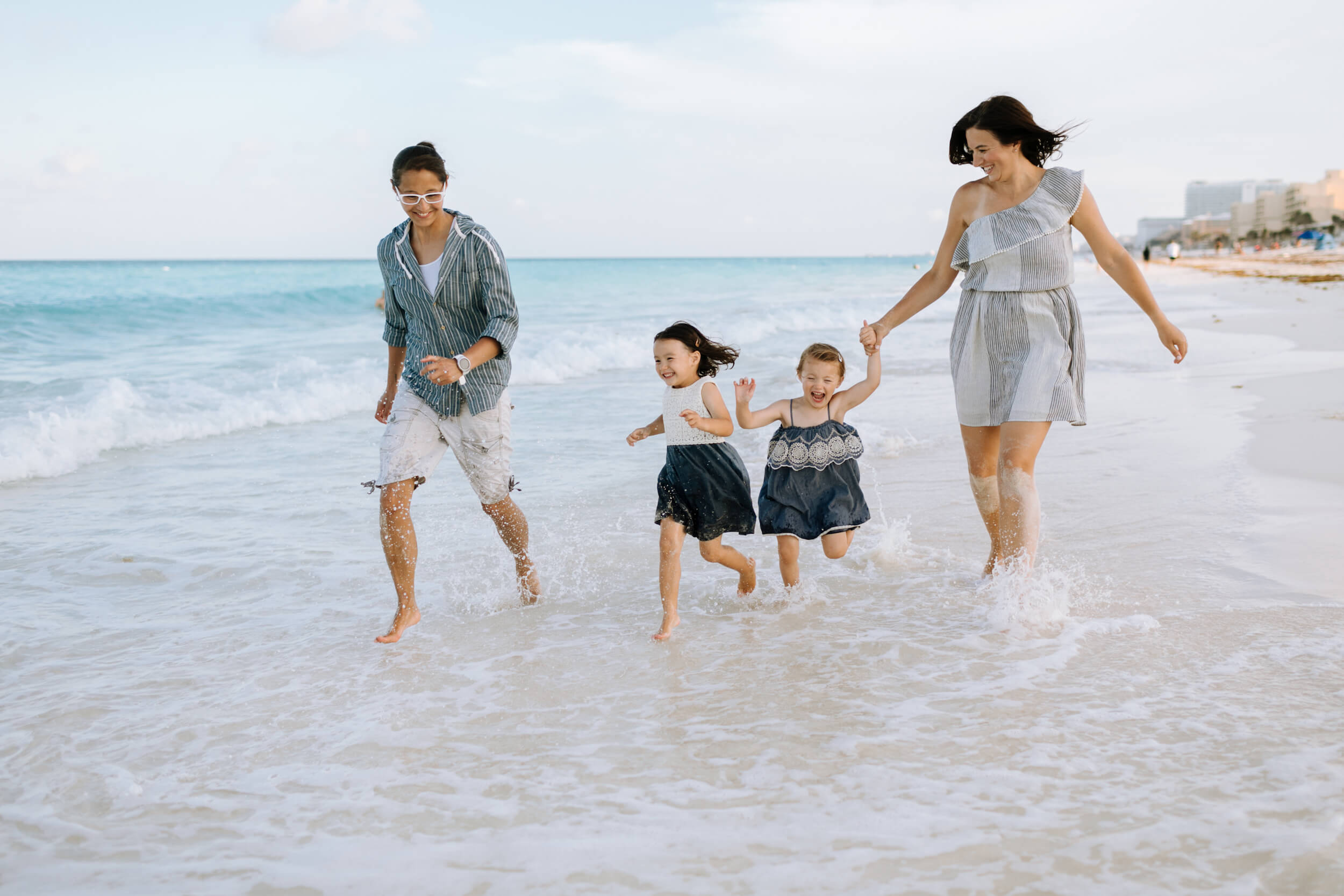Two moms and their little girls run in the surf in Cancun, Mexico.
