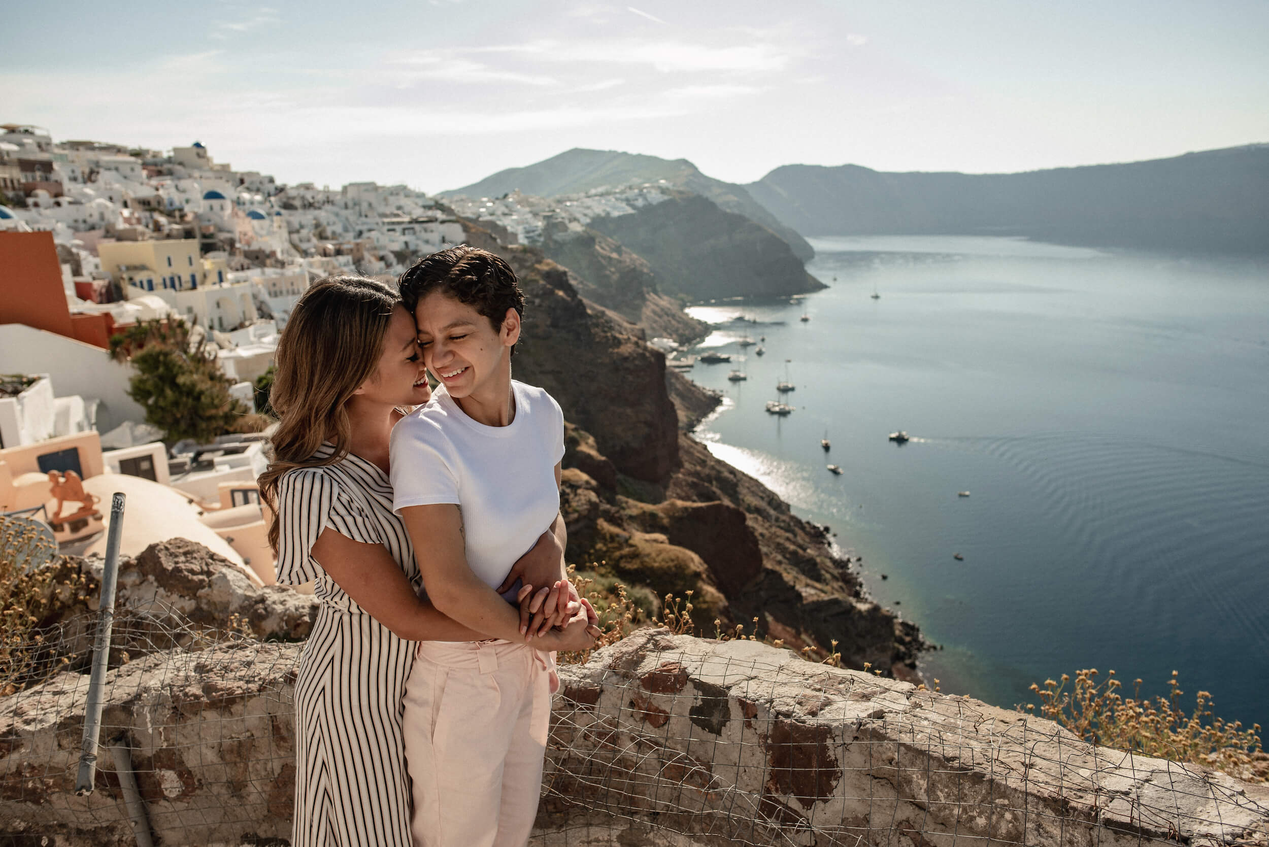 Two lovers embrace in front of the iconic blue domes in Santorini, Greece.