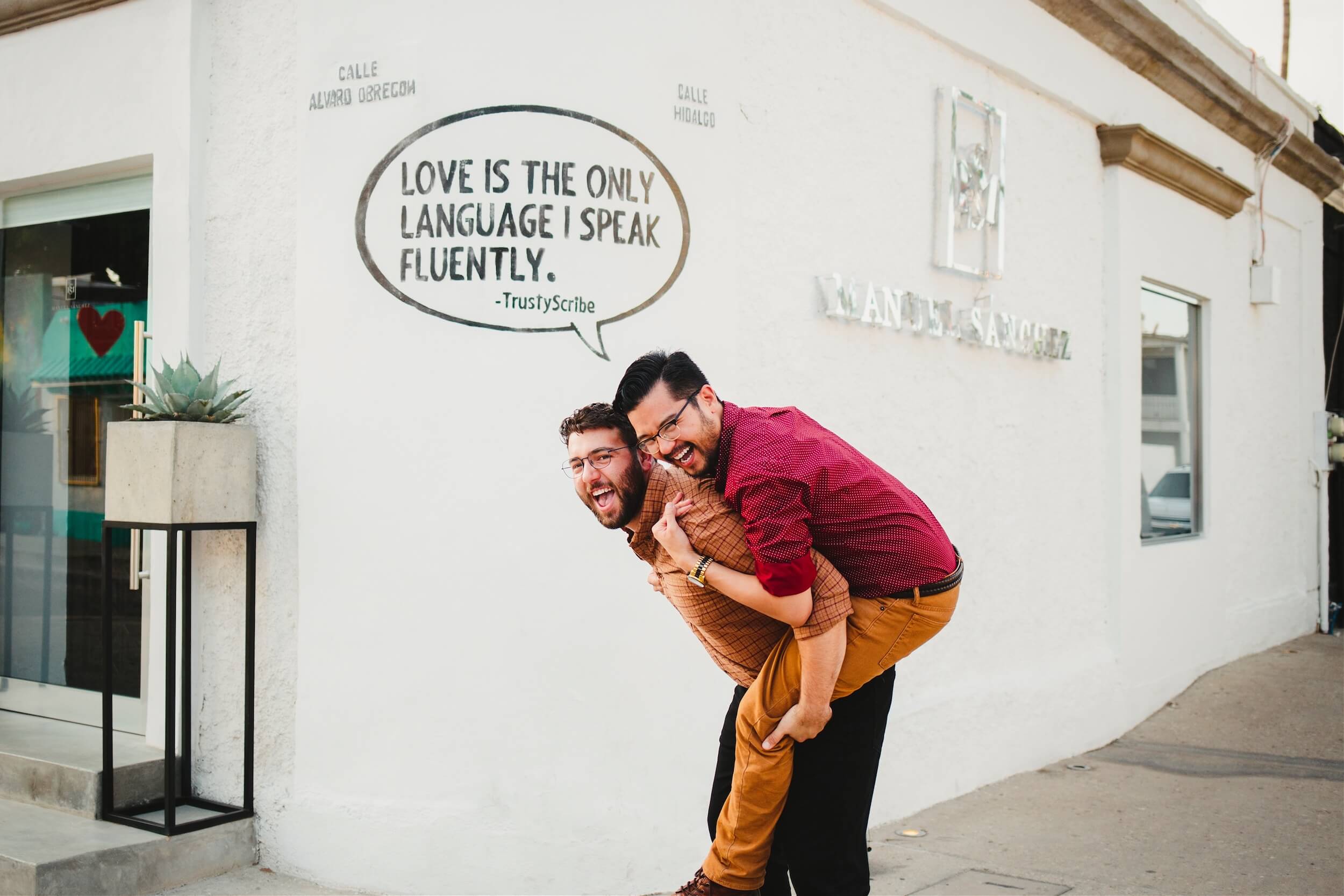 A male couple laughs in front of a painted wall in Cabo San Lucas, Mexico.
