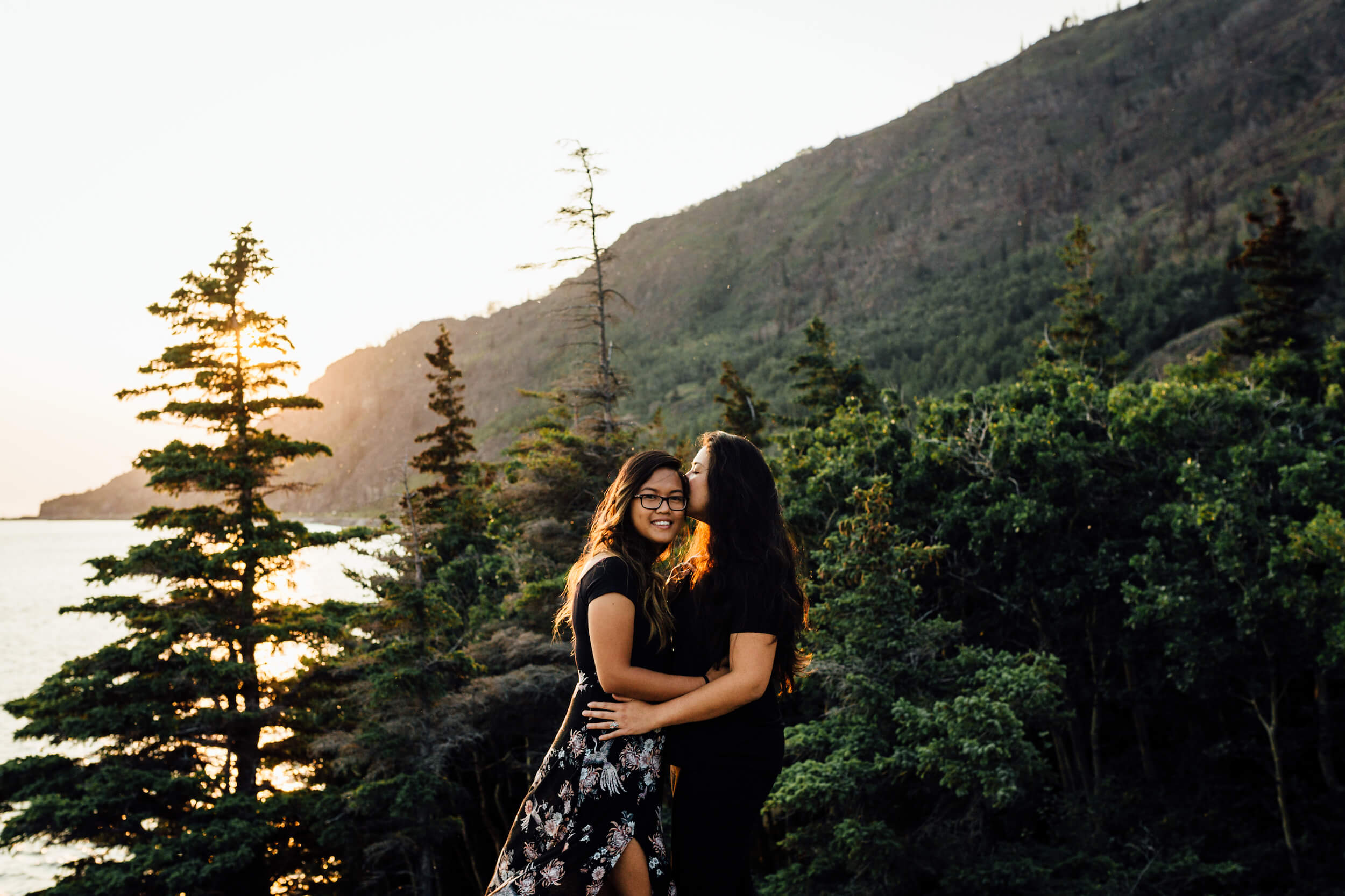 A female couple hold each other while the sun sets over the mountains in Anchorage, Alaska, USA.