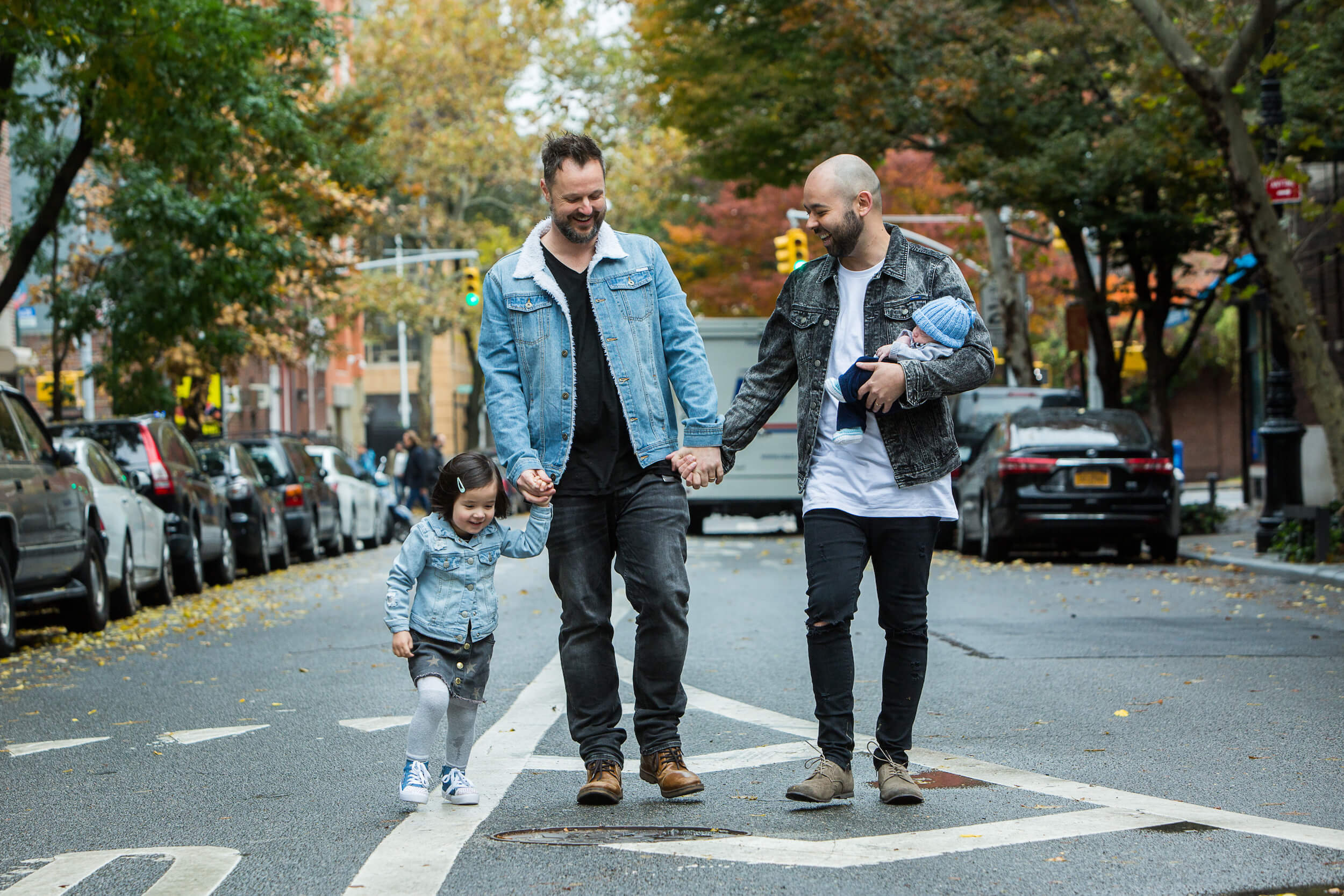 Two dads hold hands with their small children while walking along a street in New York City, USA.