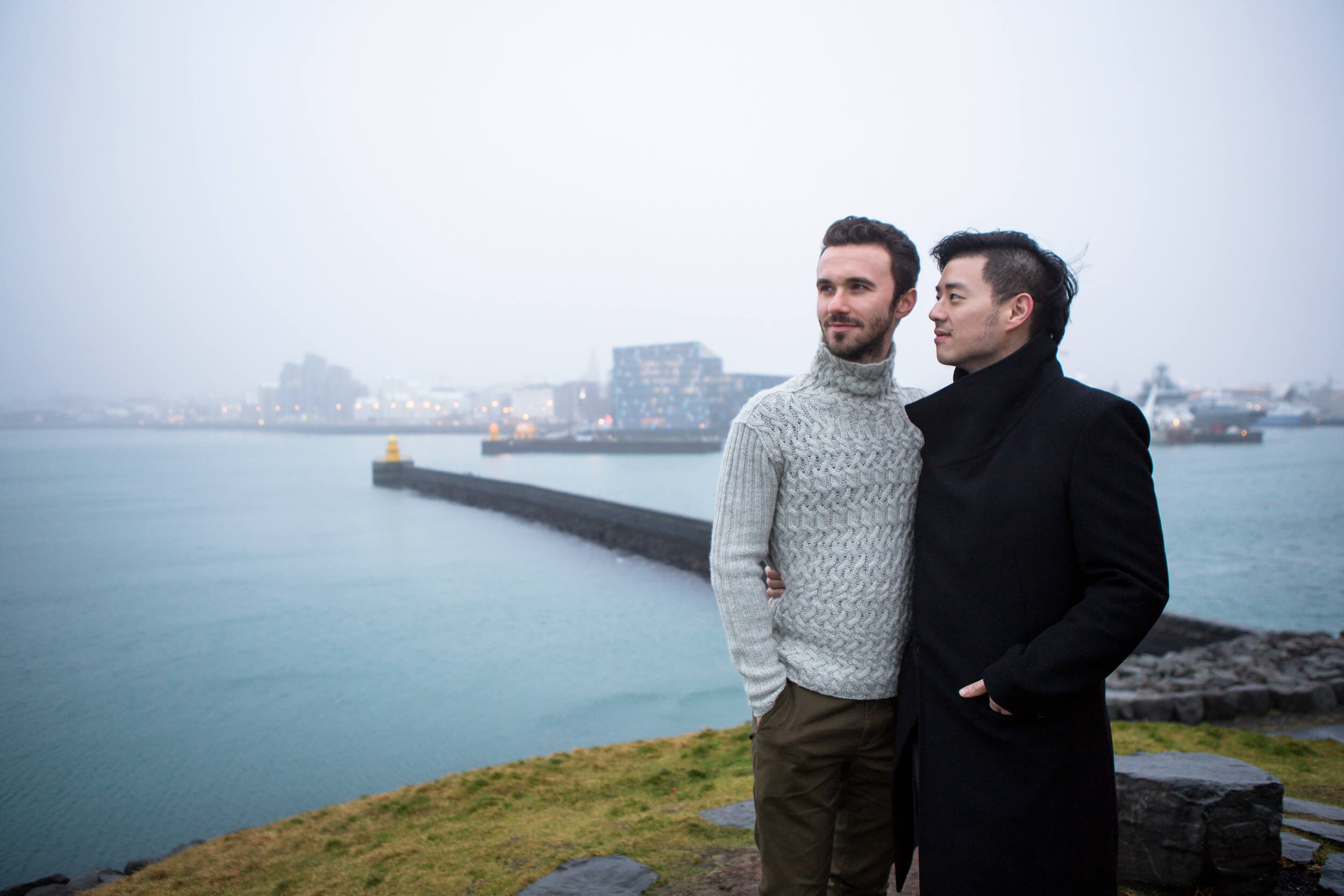 A male couple hold each other looking over the harbour in Reykjavik, Iceland.