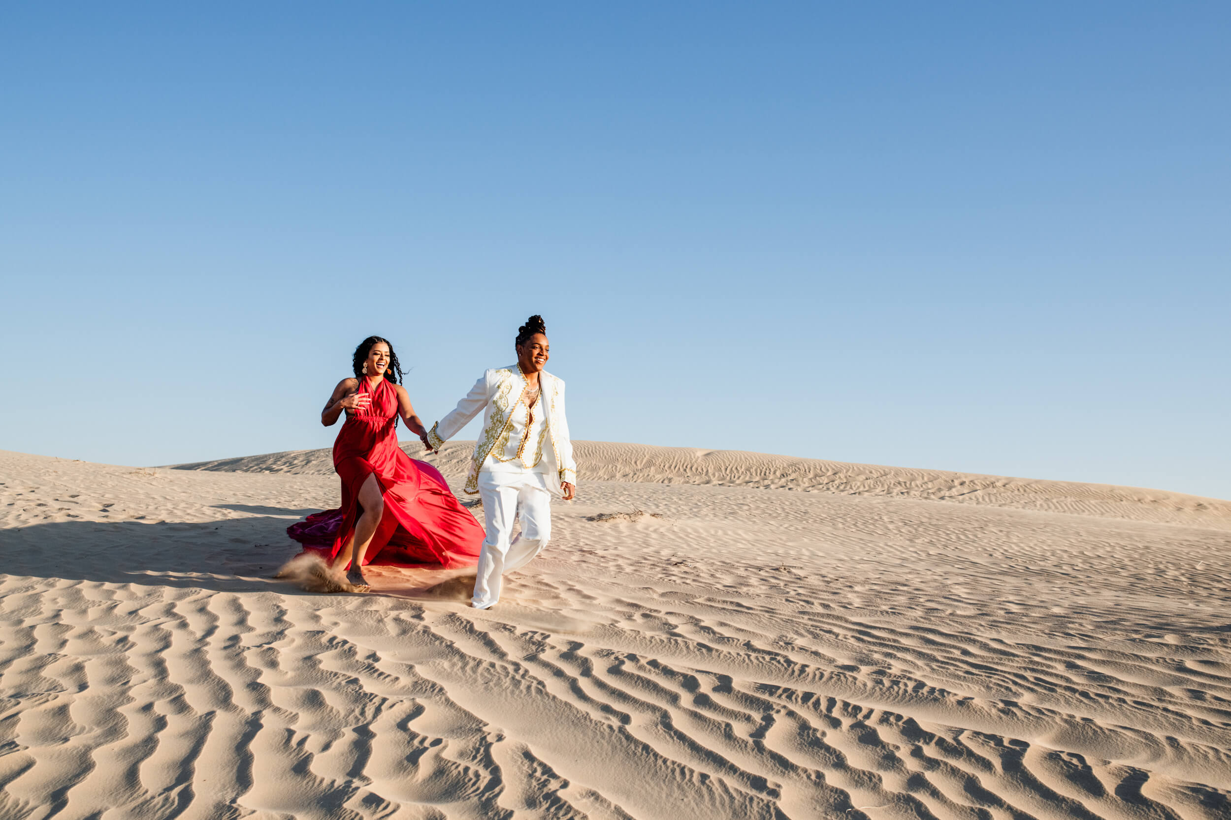 A Lesbian couple hold hands and laughing while running across the sand dunes in Dubai, UAE. 