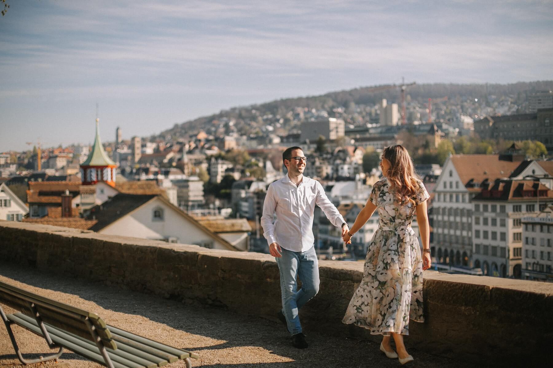 A couple holds hands looking at each other on a sunny say at the Lindenhof Lookout in Zurich.
