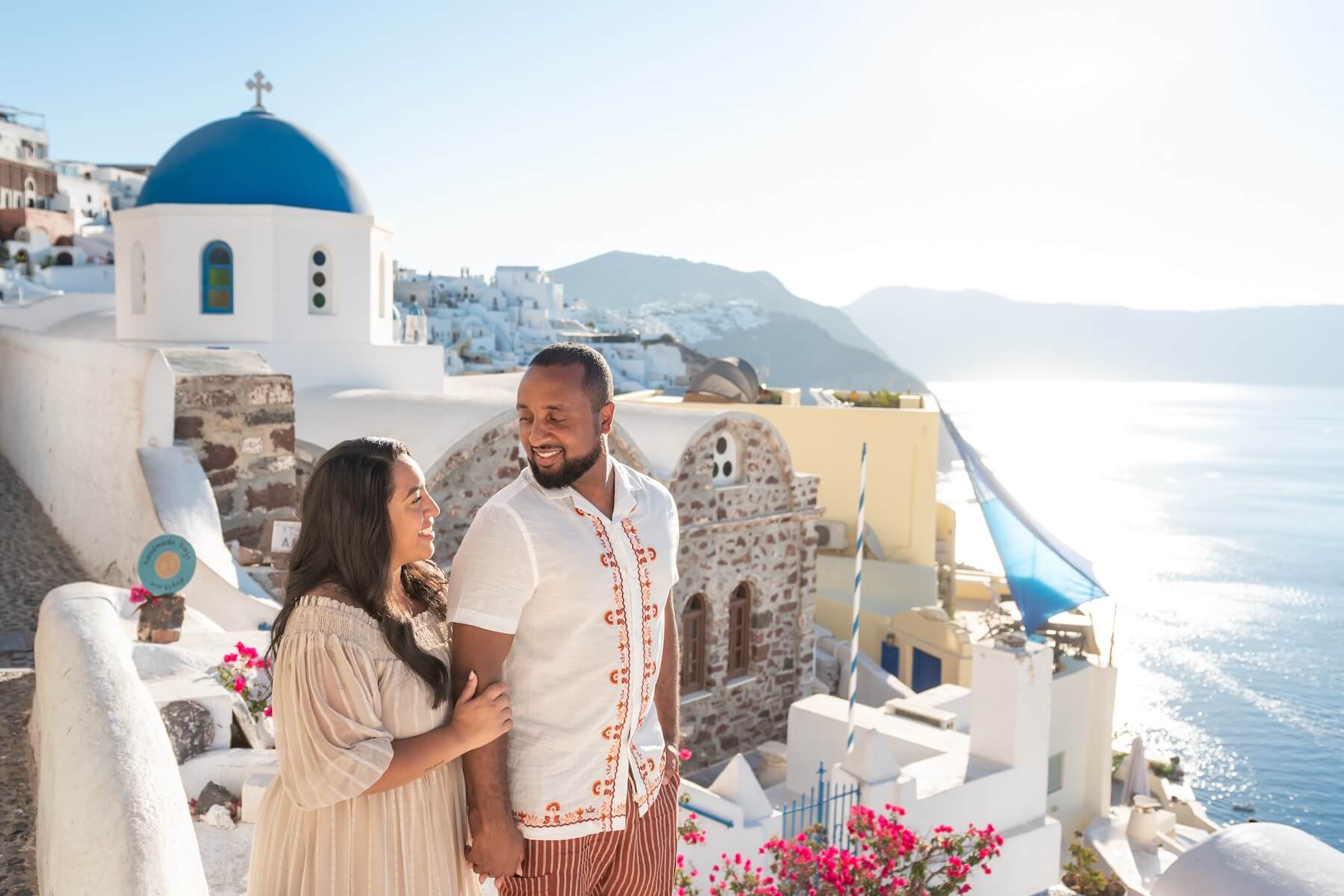 A woman holds her partner’s arm as they walk along a path in Santorini.