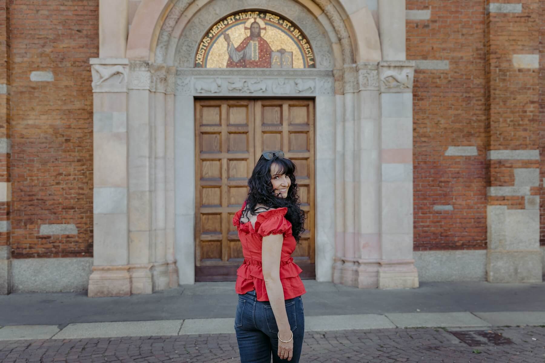 A woman looks back at the camera smiling wearing a red shirt in Milan.
