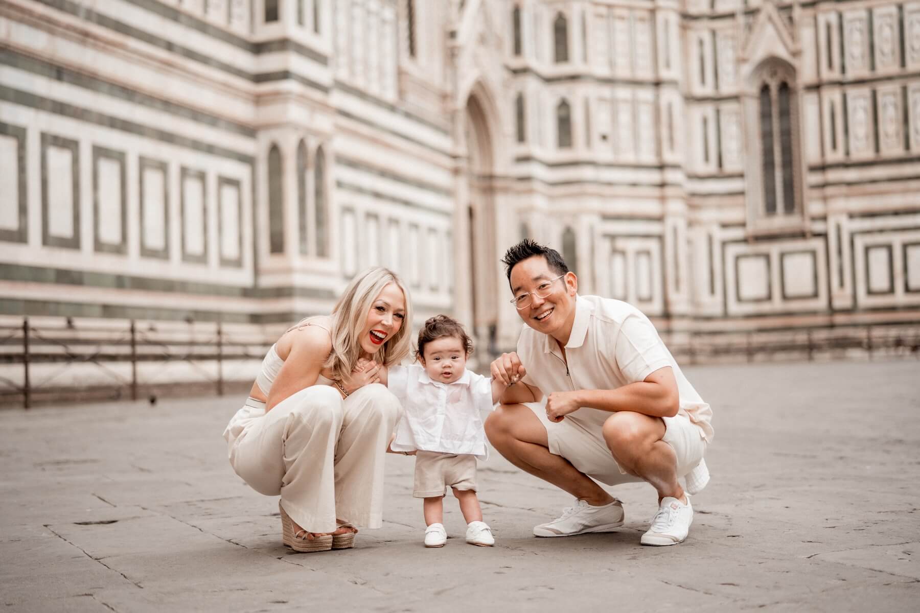 A couple crouches down and hold their young son by his hands in front of the Duomo in Florence, Italy.