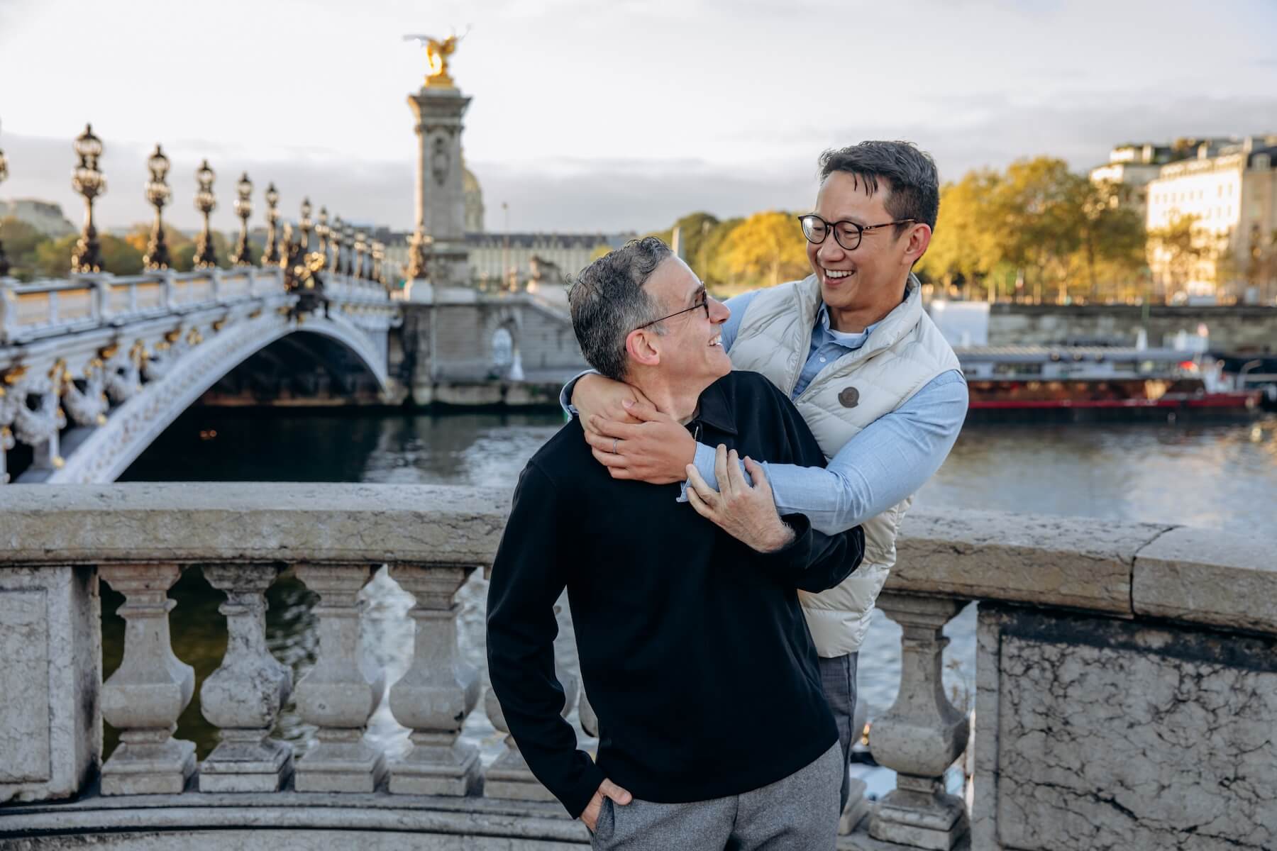 A man wraps his arms around his partner while they smile in Paris.