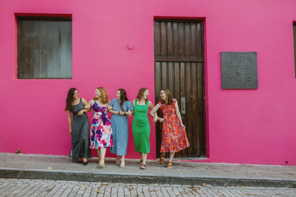 Ladies linking arms in front of a hot pink wall in San Juan Puerto Rico on a friends photoshoot with Flytographer.