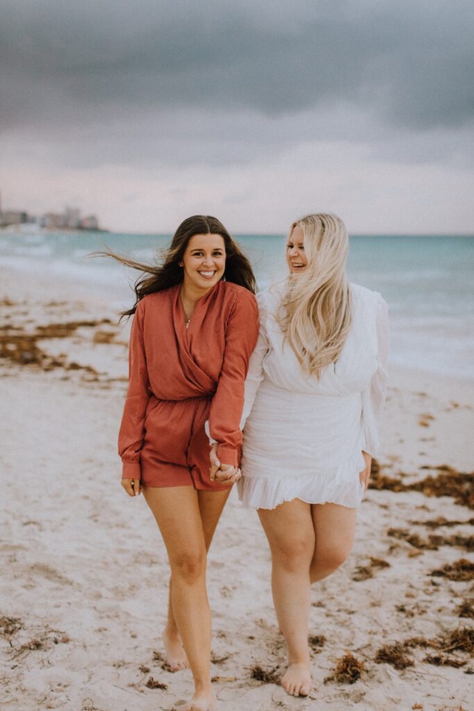Two friends walking and laughing on the beach  in Miami, Florida at South Pointe Park & Beach on a bachelorette photoshoot with Flytographer.